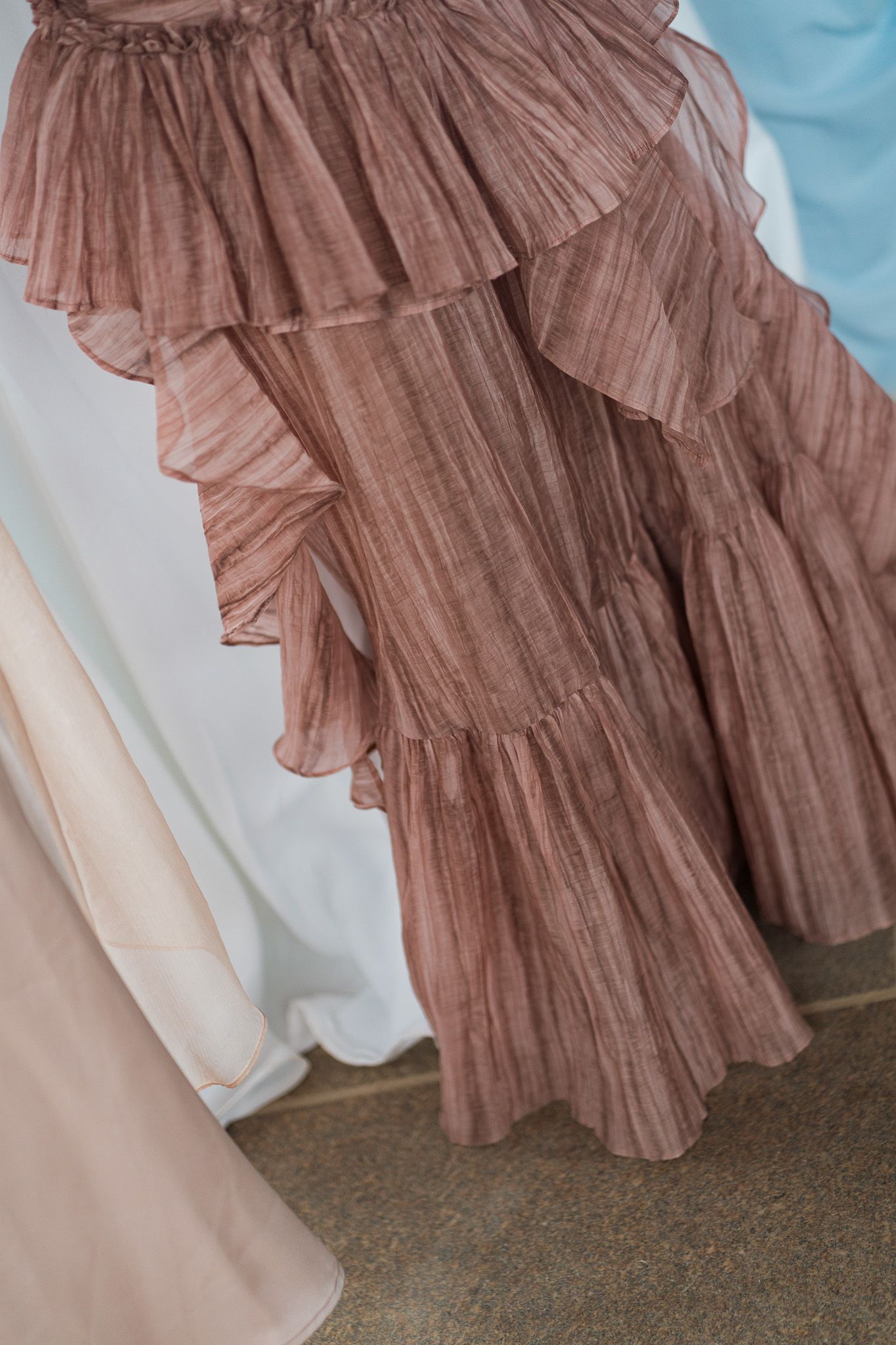 Layered dusty rose ruffled chiffon skirt gown displayed among other formal dresses in a bridal boutique.