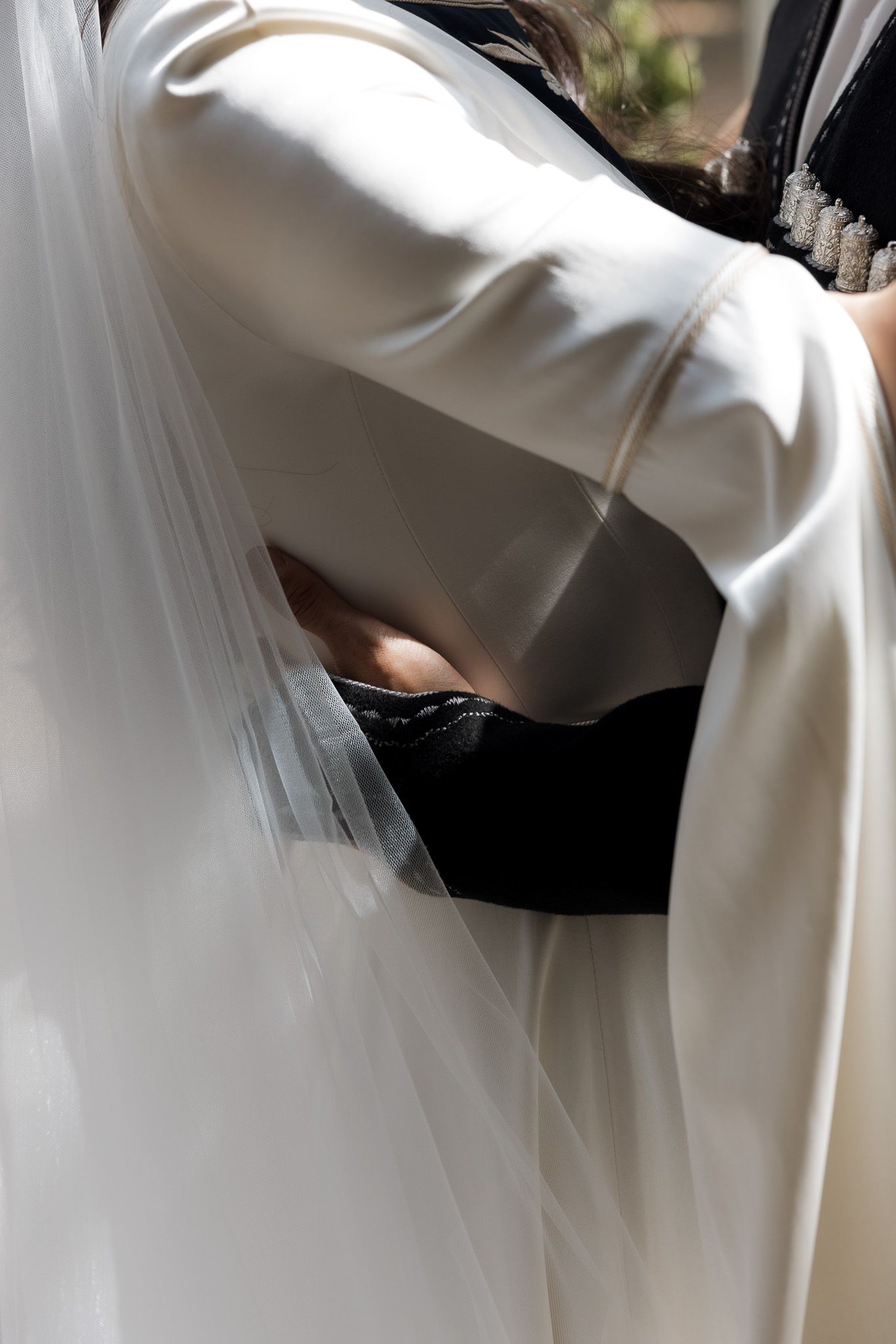 Close-up of a bride in a white wedding gown and veil embracing someone in a black outfit.