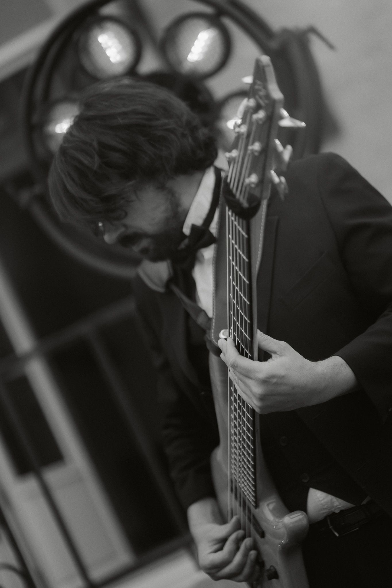Black and white photo of a man playing electric guitar, wearing a suit, with stage lights in the background.