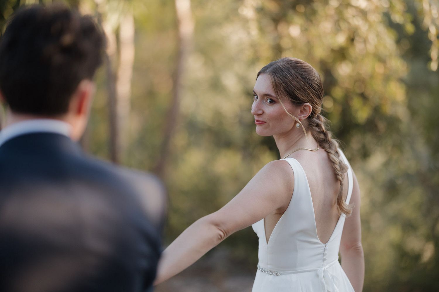 A bride in a white wedding dress poses outdoors among trees during a sunset photo session.