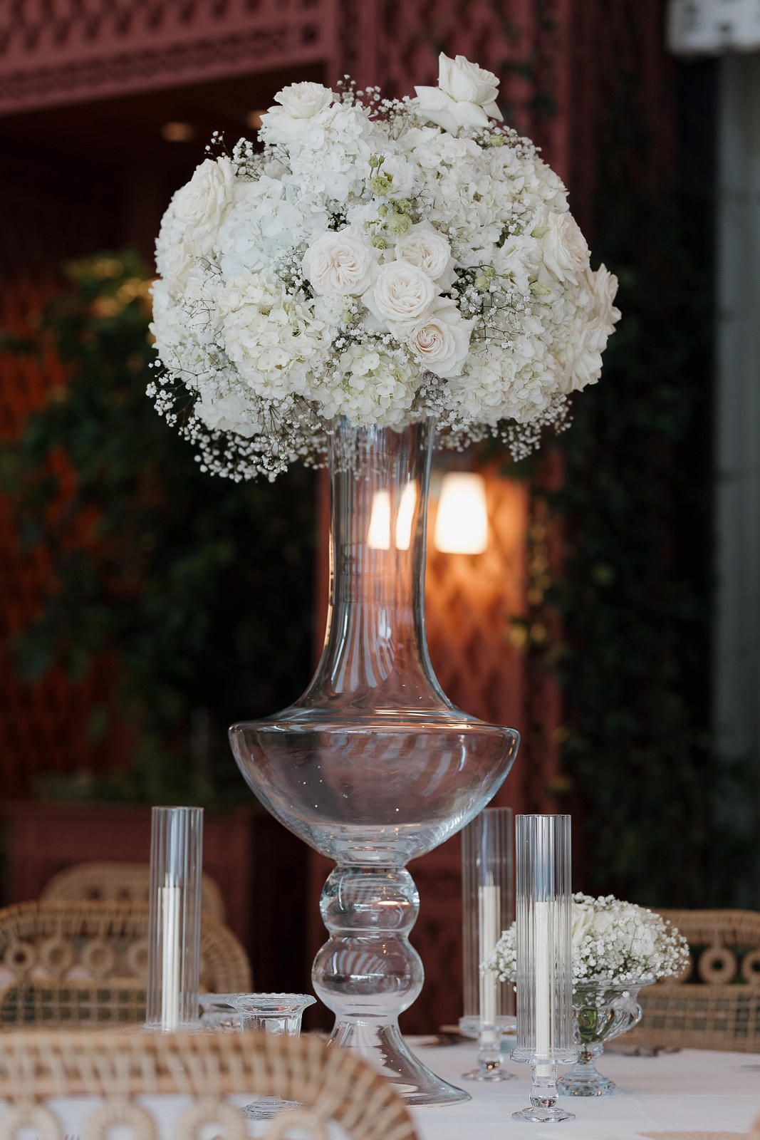 Elegant white floral centerpiece arrangement with baby's breath in a tall glass vase on a formal table setting.