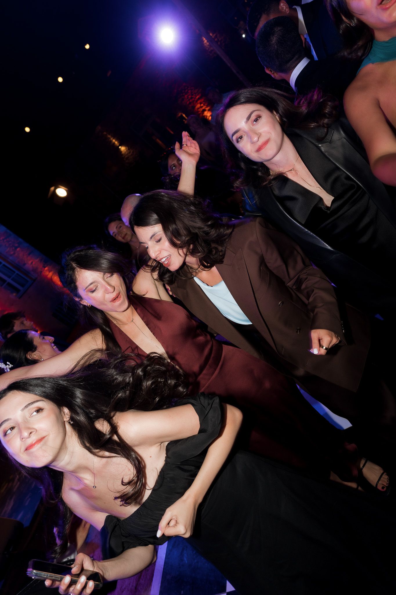 Group of young women dancing and socializing at a nightclub party with colorful lights in background.
