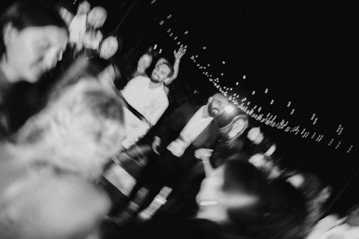 Black and white photo of people dancing and celebrating at a lively nighttime outdoor party event.