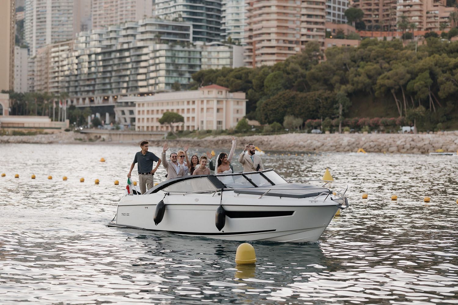 A white speedboat cruises across calm waters near a coastal cityscape with high-rise buildings in the background.