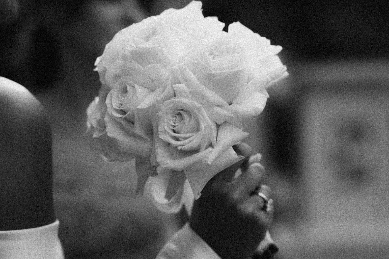 A black and white photograph of elegant white roses in a bouquet with soft bokeh background effect.