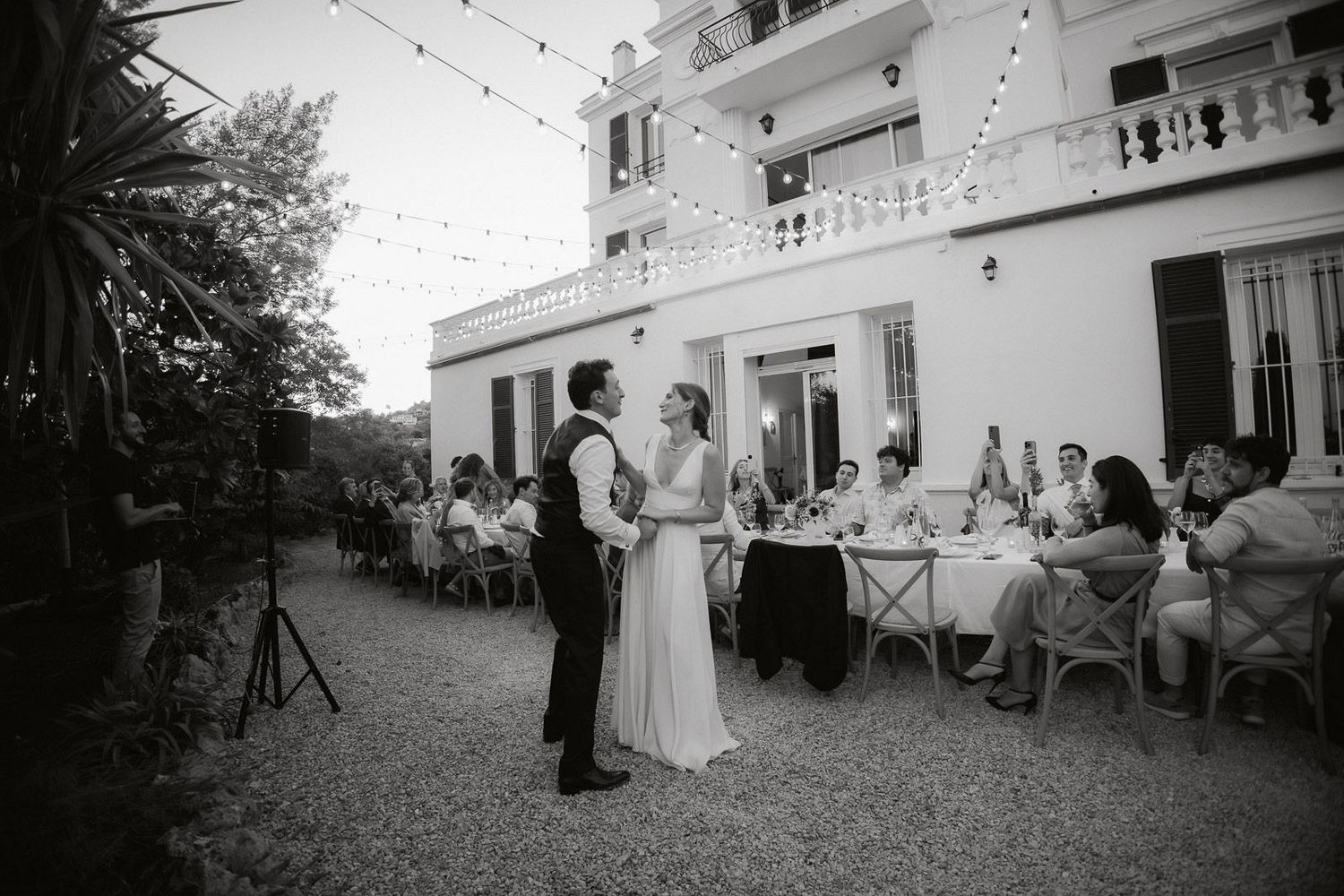 A series of black and white wedding photos showing outdoor reception scenes with string lights and elegant decor.