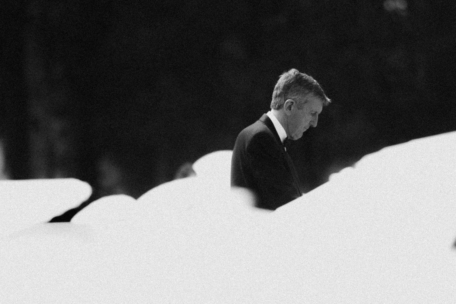 Black and white photo of a man in a suit standing pensively among snow-covered mounds in a winter landscape.