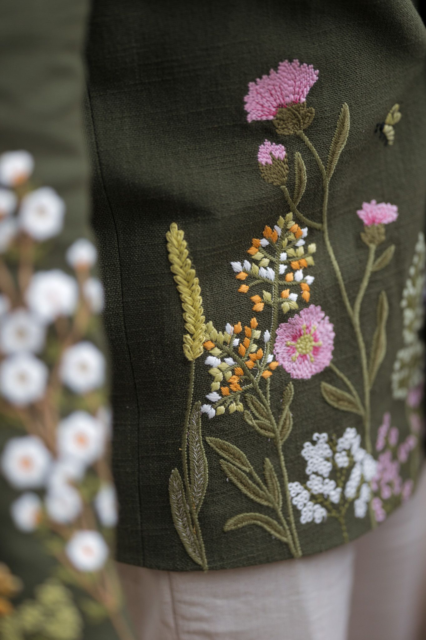 Close-up of dark green fabric with colorful floral embroidery featuring pink, white, and orange wildflowers.
