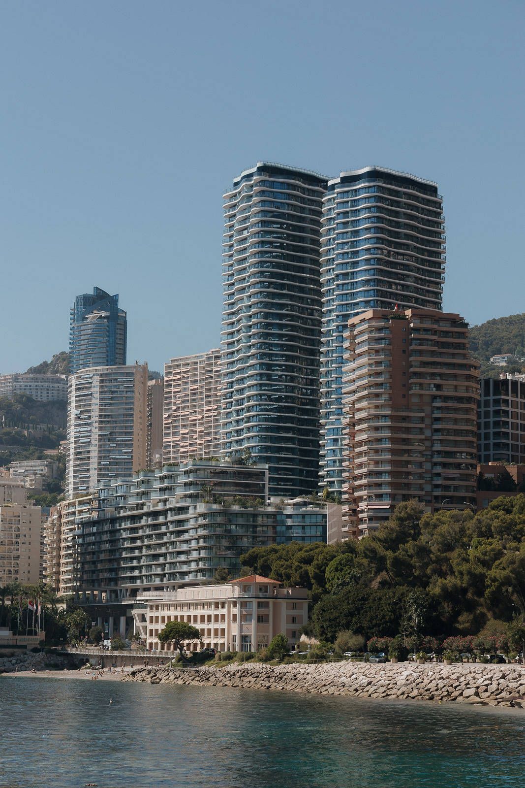 Modern high-rise apartment buildings line the waterfront of Monte Carlo with a rocky beach below.