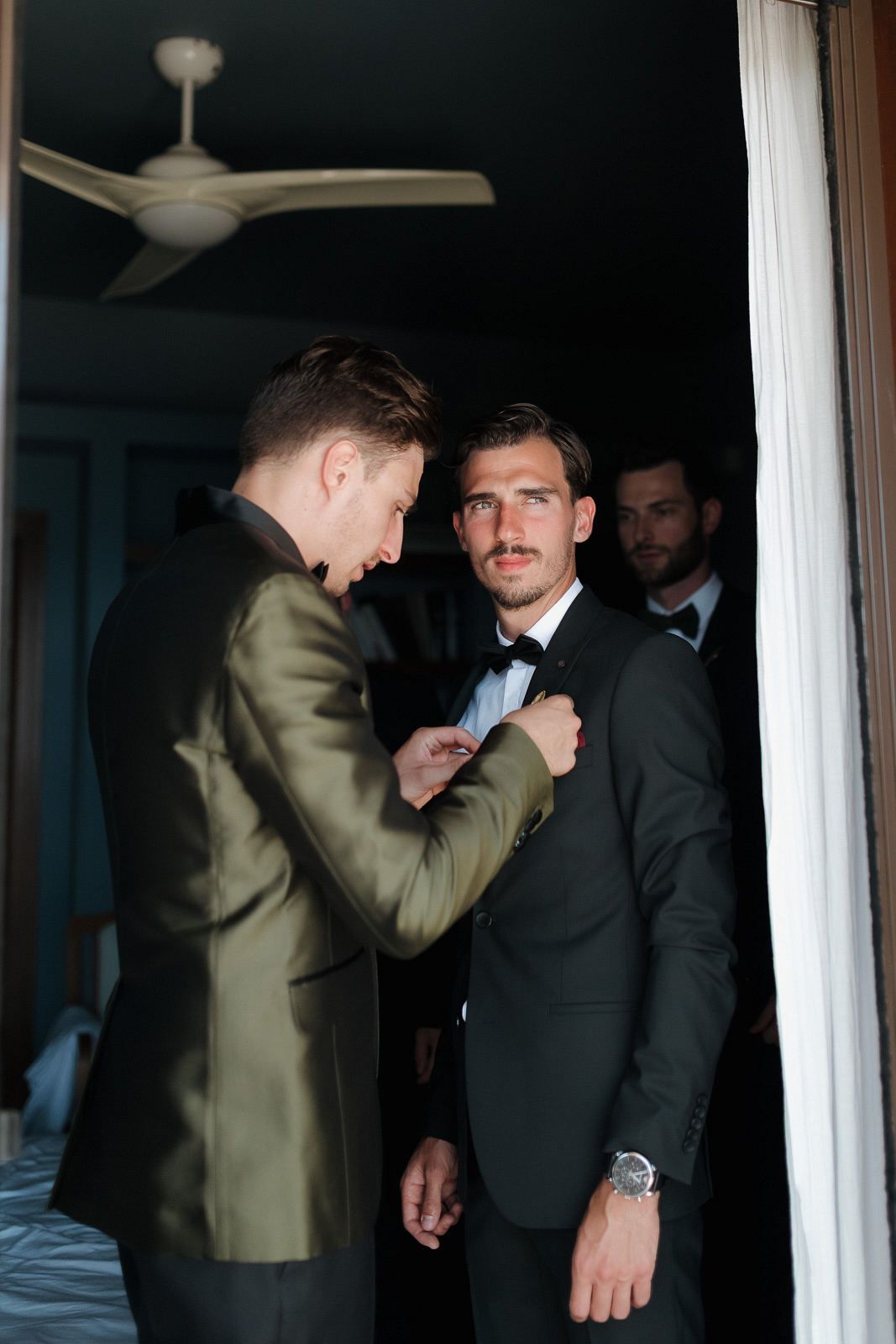 Two men in formal attire interact in a dimly lit interior space with white columns visible in the background.