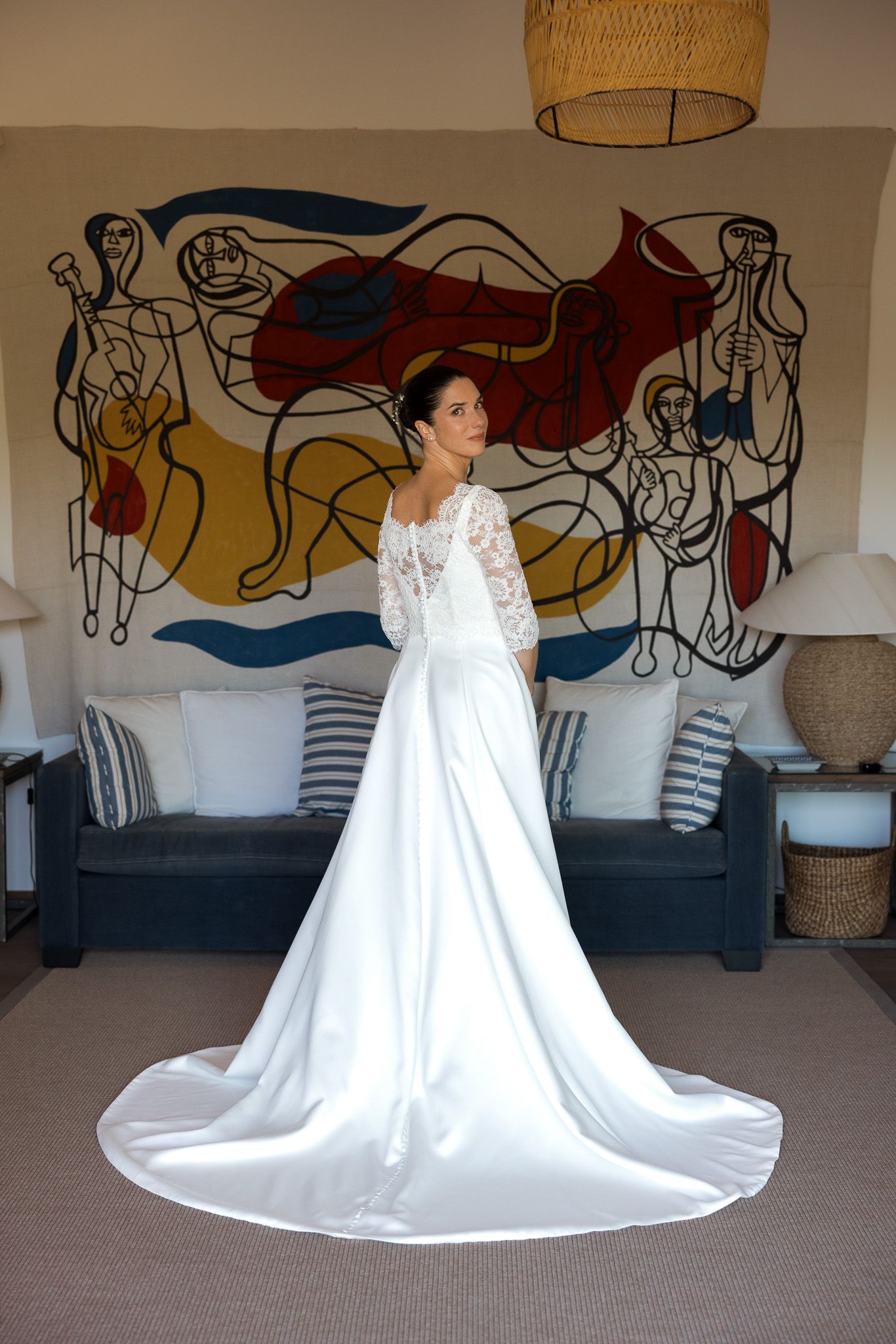 Bride in elegant white lace long-sleeve wedding gown with cathedral train poses in front of colorful abstract wall mural.