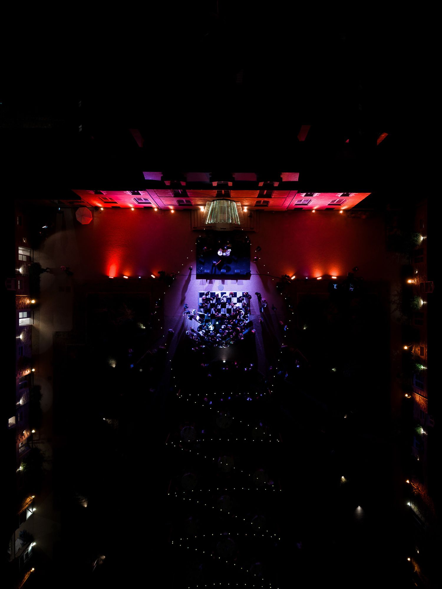 Aerial view of a concert hall with red and purple stage lighting illuminating performers and audience below.