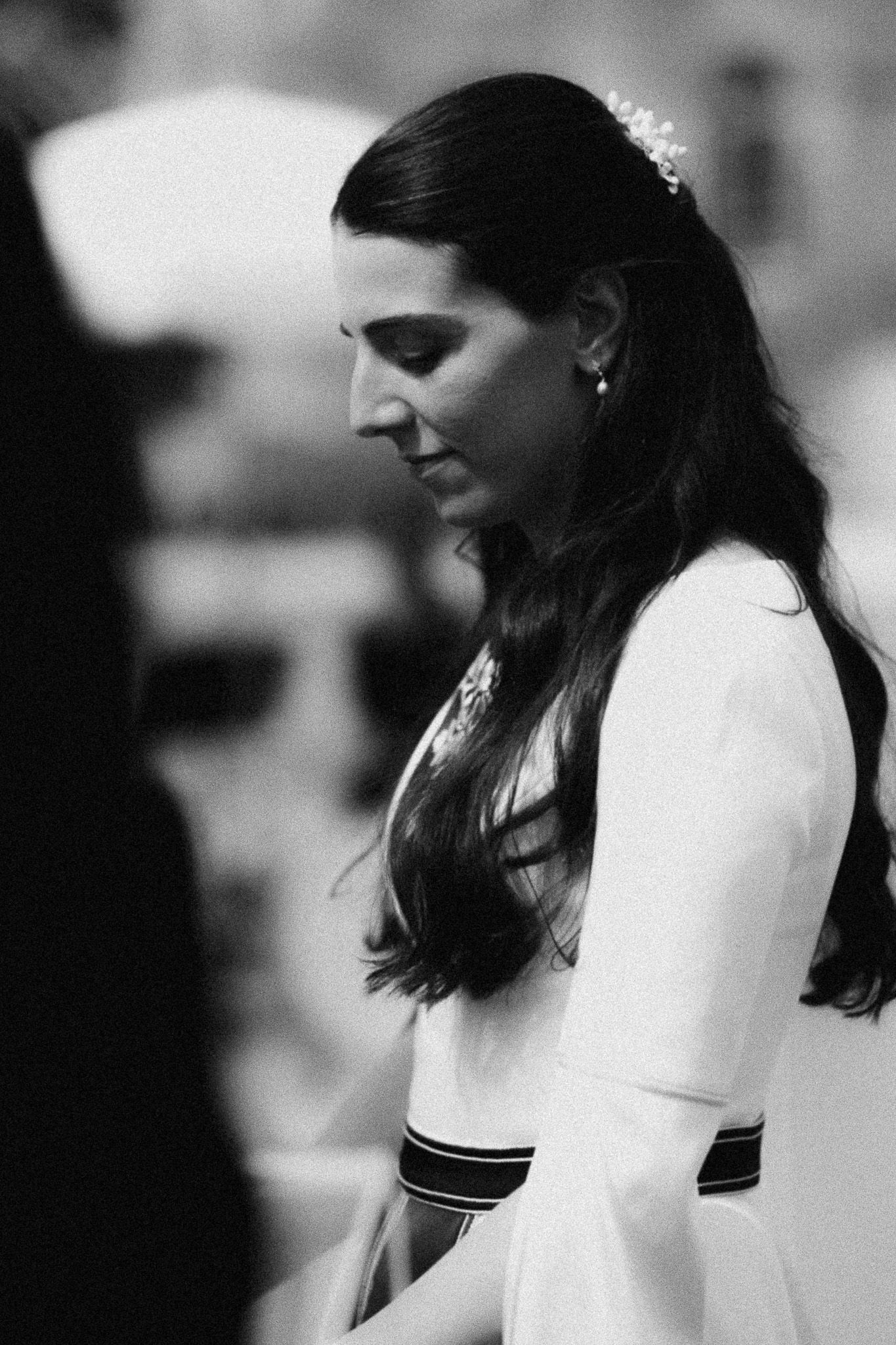 Black and white portrait of a bride with long dark hair and floral hair accessory, wearing a white dress, looking down.