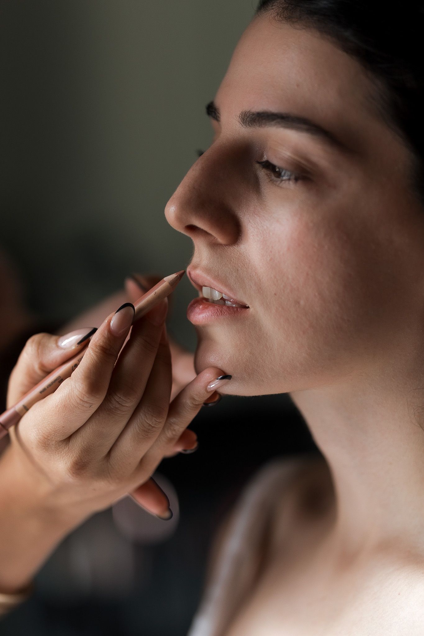 A makeup artist applying lip liner to a young brunette woman during a professional beauty session.