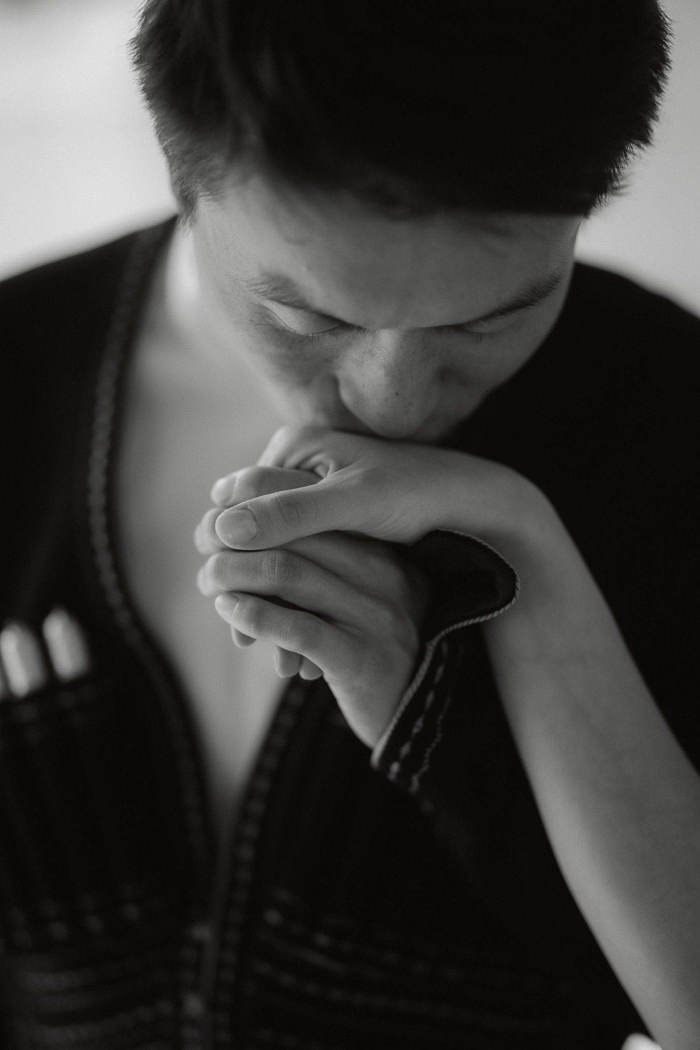 Black and white photo of a person with clasped hands raised to their lips in a prayer or contemplative pose.