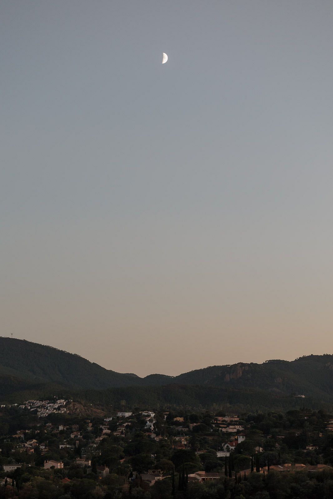 Panoramic view of hillside homes nestled among mountains at dusk with a soft gradient sky.