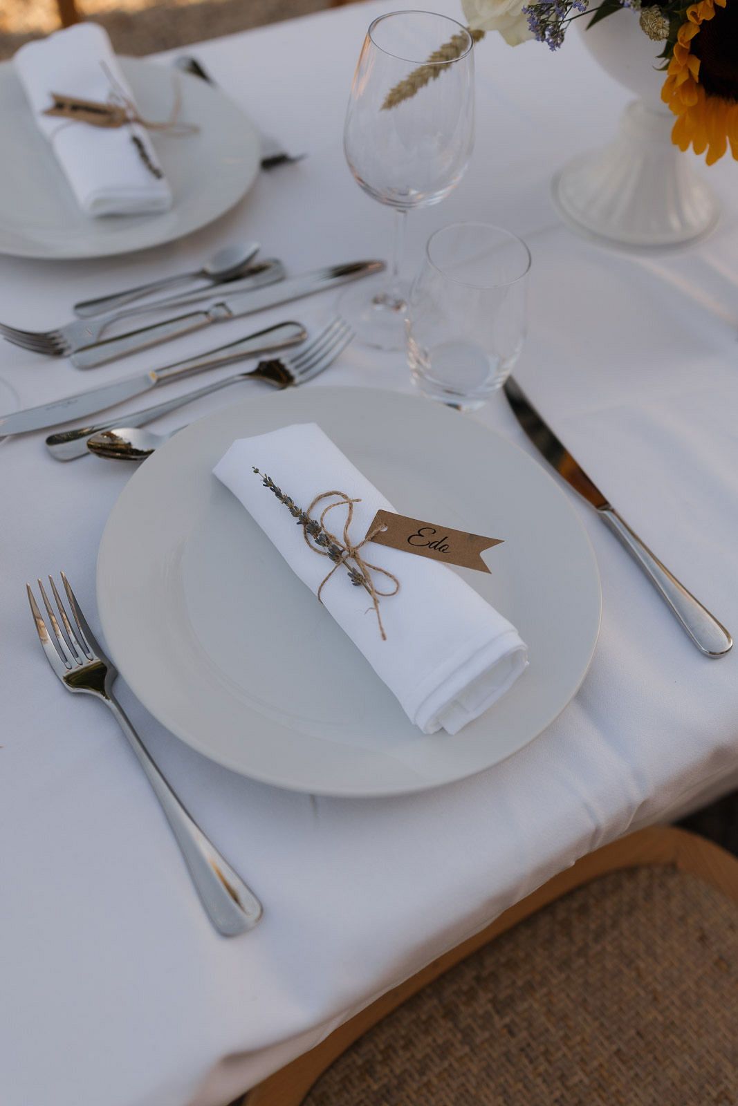 Elegant table settings with white plates, silverware, and napkins tied with twine on a crisp white tablecloth.