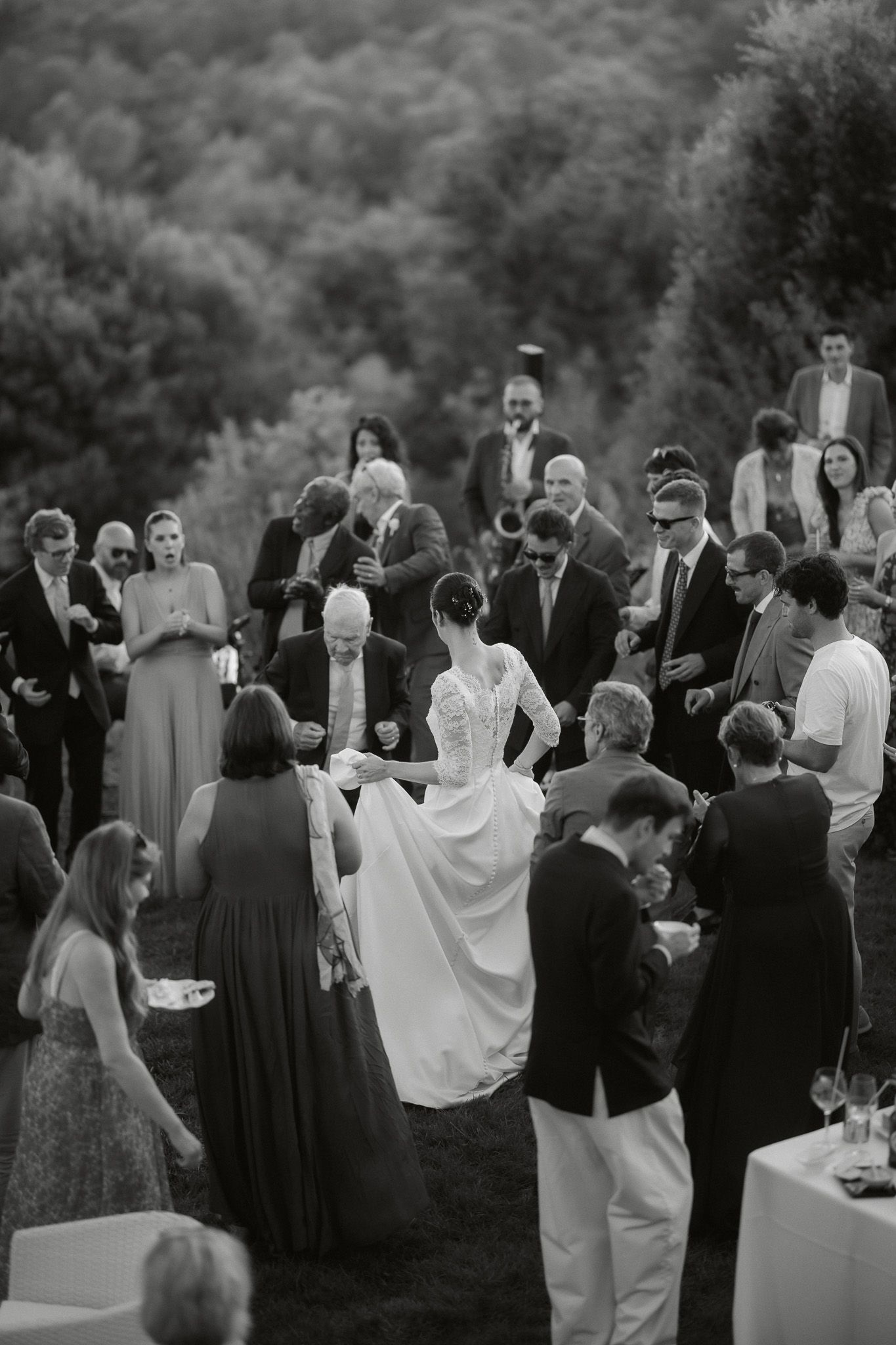 Black and white outdoor wedding reception with bride in lace gown mingling among elegantly dressed guests.