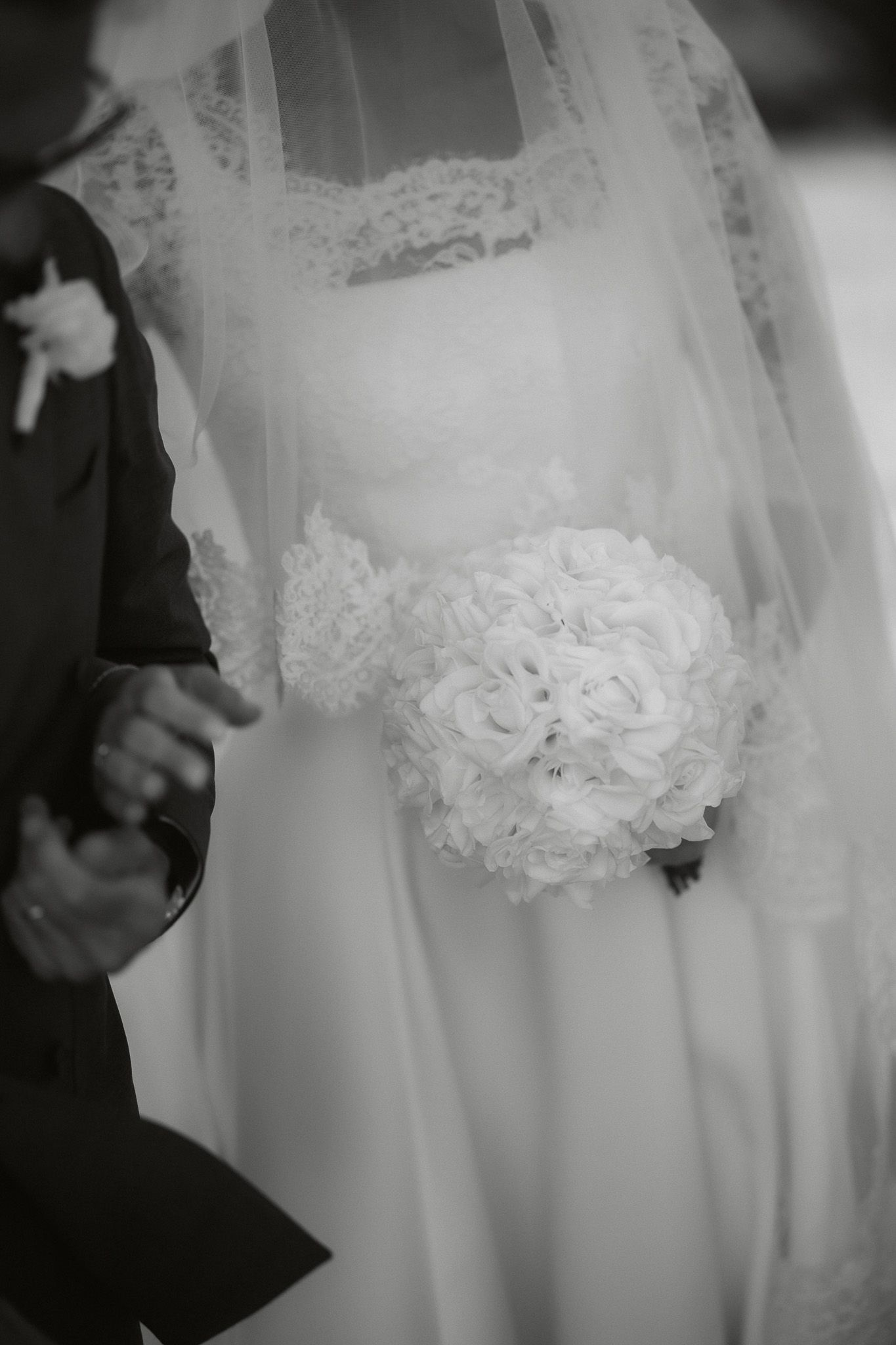 Black and white wedding photo of bride holding white rose bouquet while standing next to groom in dark suit.