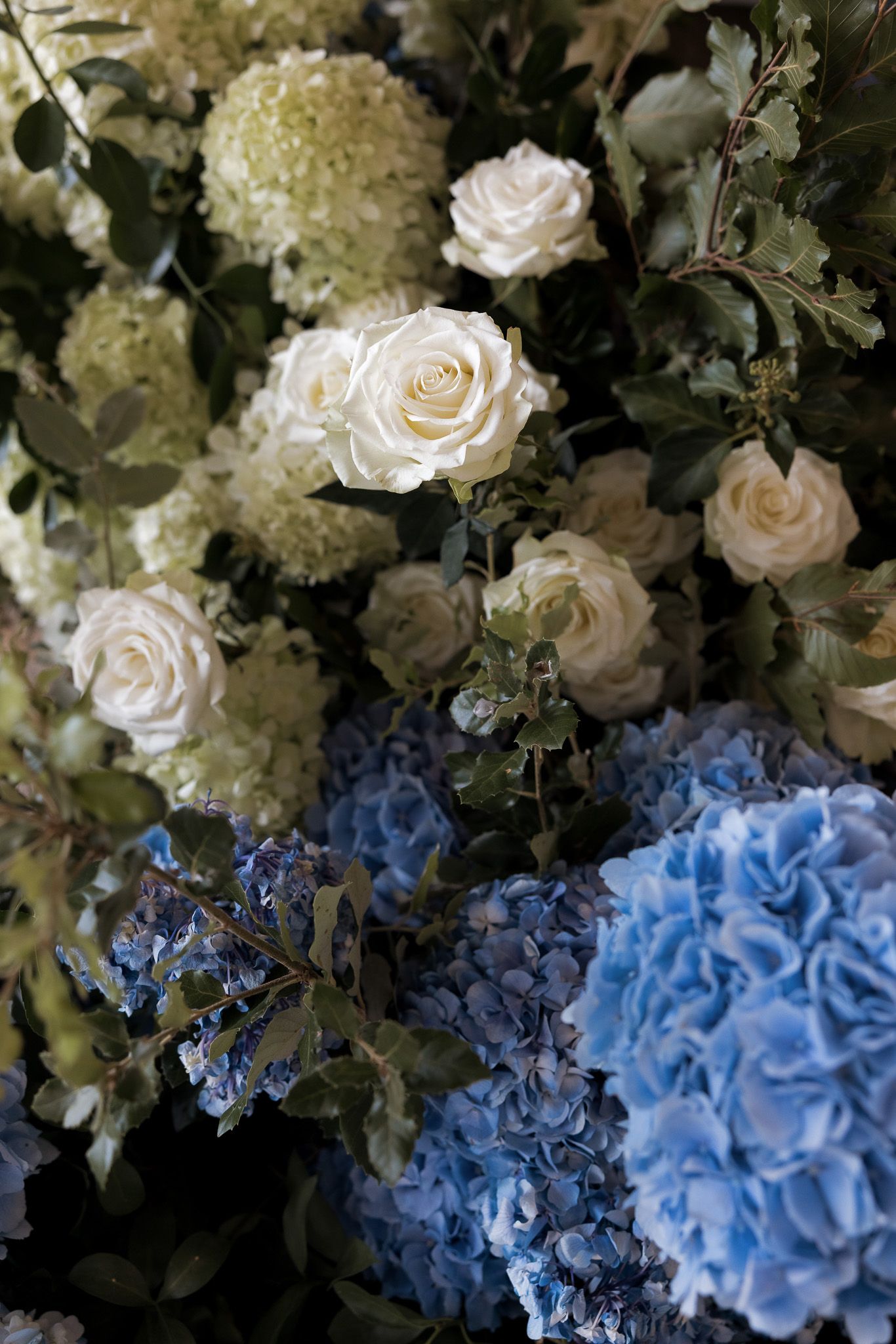 Elegant floral arrangement featuring white roses, green hydrangeas, and blue hydrangeas with lush foliage.