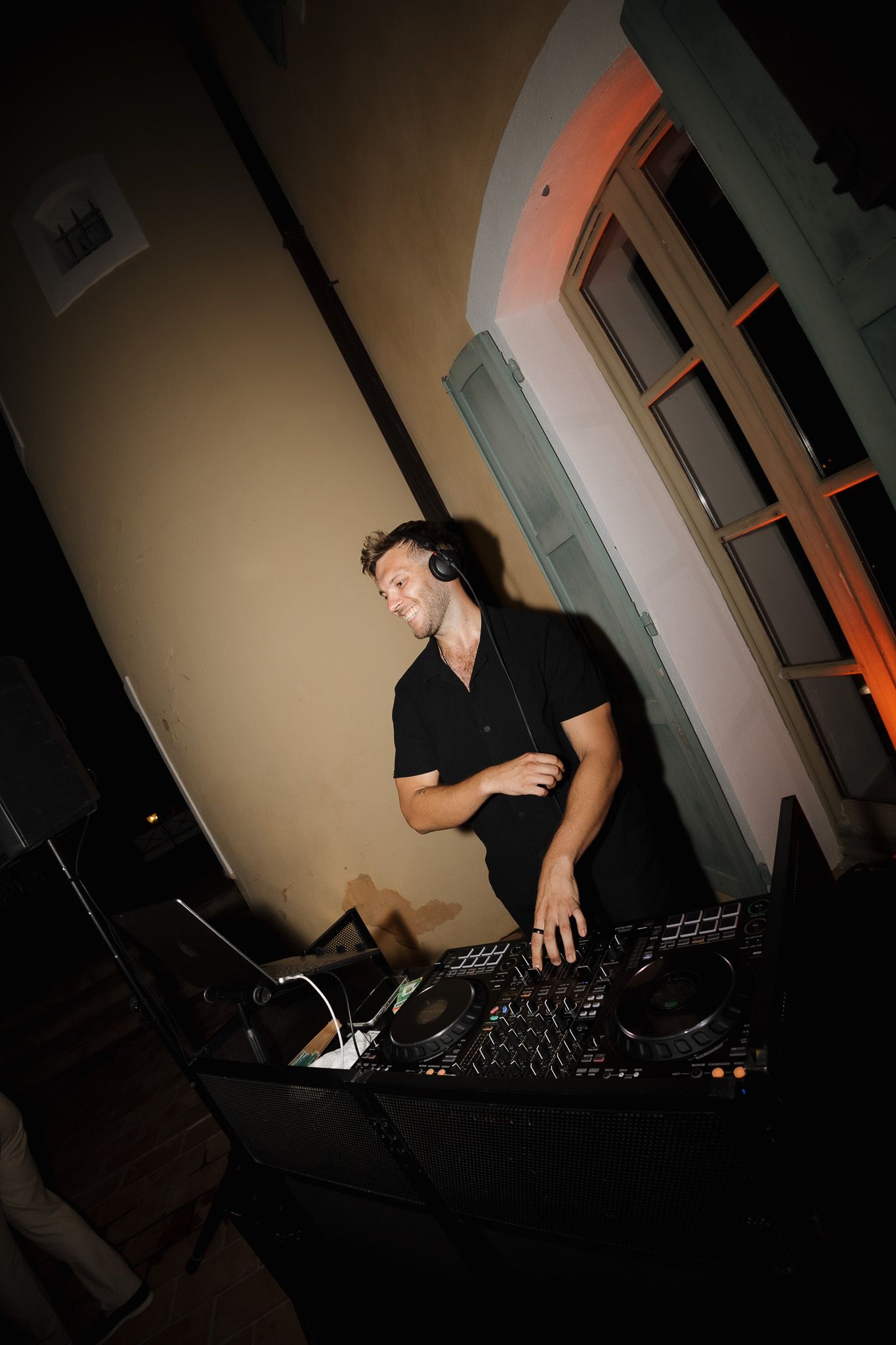 DJ mixing music at a wedding reception, wearing headphones and black shirt indoors.