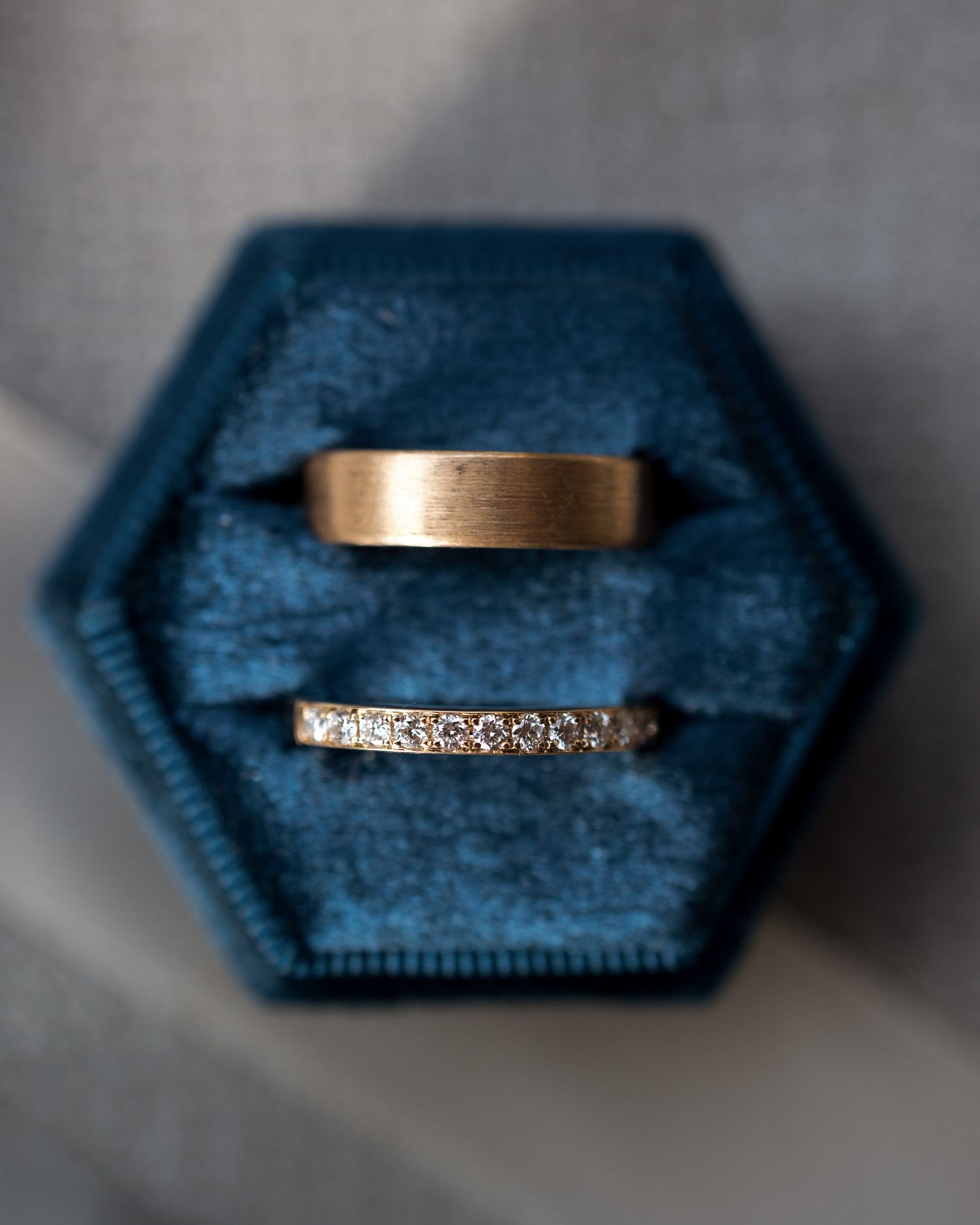 Two wedding rings in a blue velvet hexagonal ring box, one gold band and one diamond eternity band.