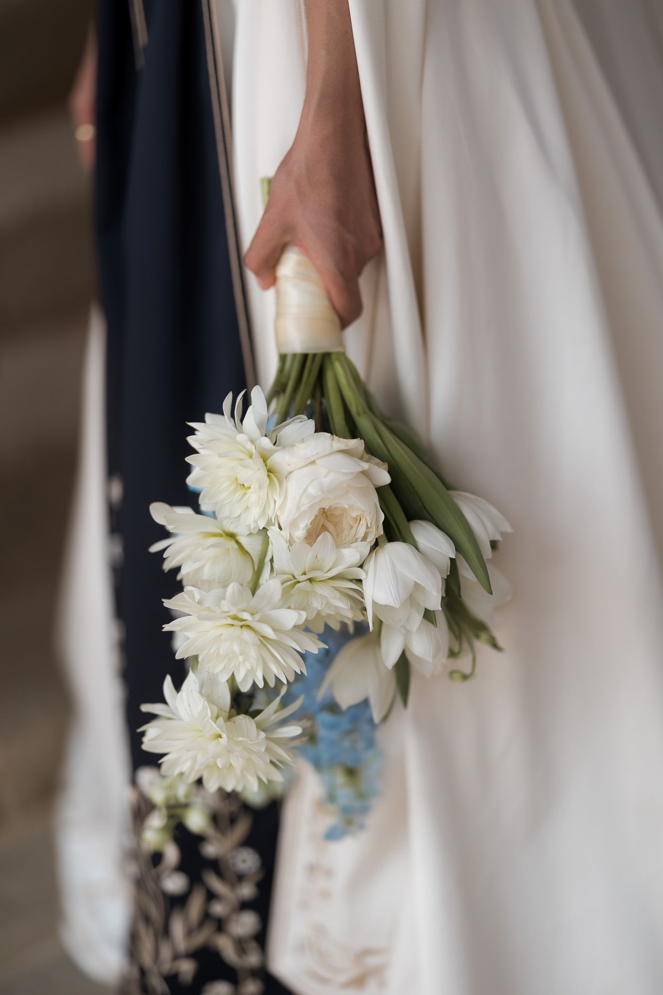 Bride holding a white wedding bouquet of tulips and chrysanthemums, draped against a flowing white gown.