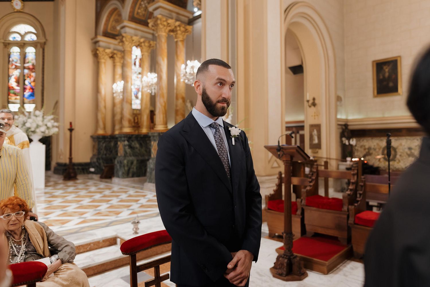 Elegant church interior with white columns, red carpet aisle, and stained glass windows during a wedding ceremony.