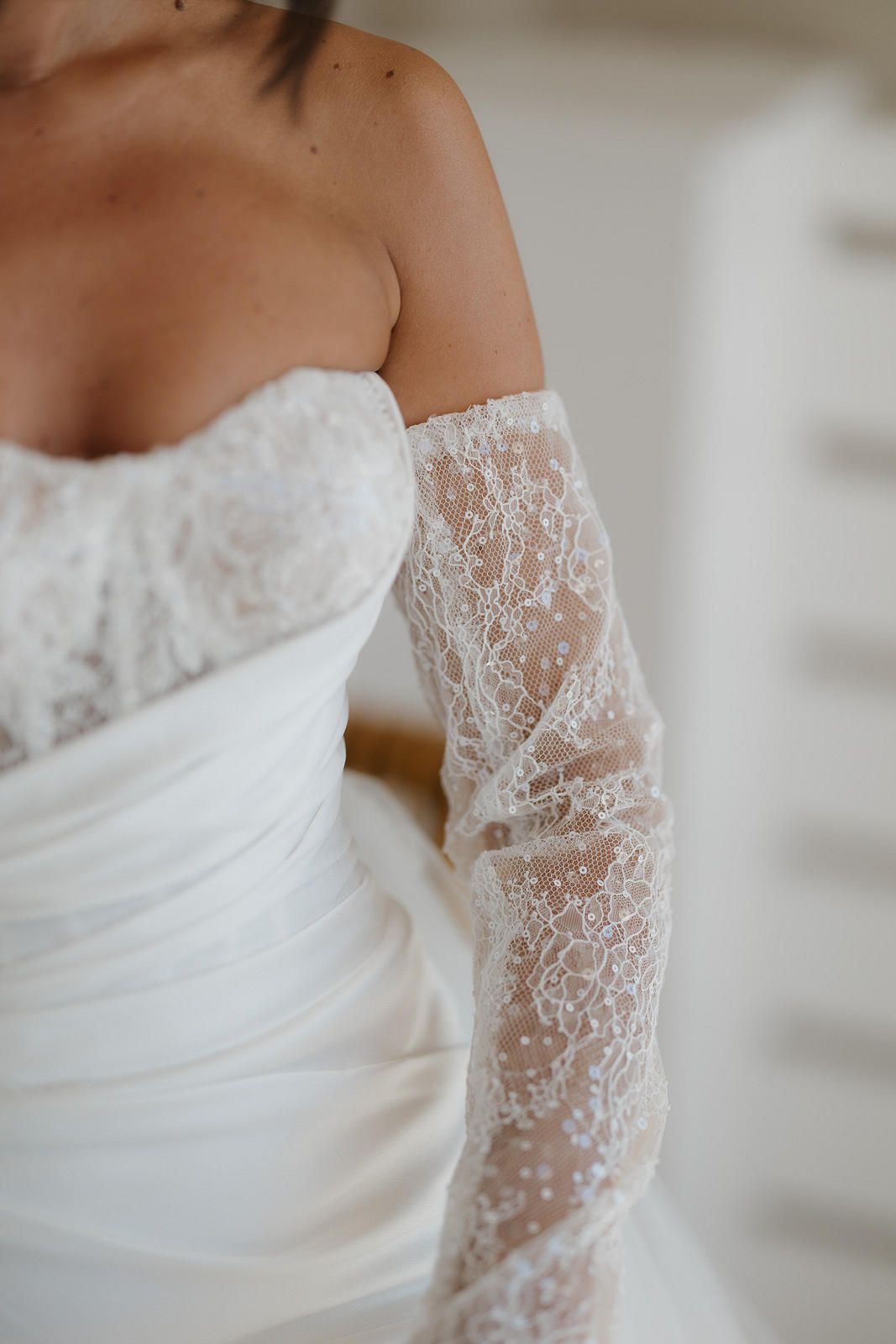 Close-up details of a white lace wedding dress sleeve with delicate floral patterns and sheer fabric.
