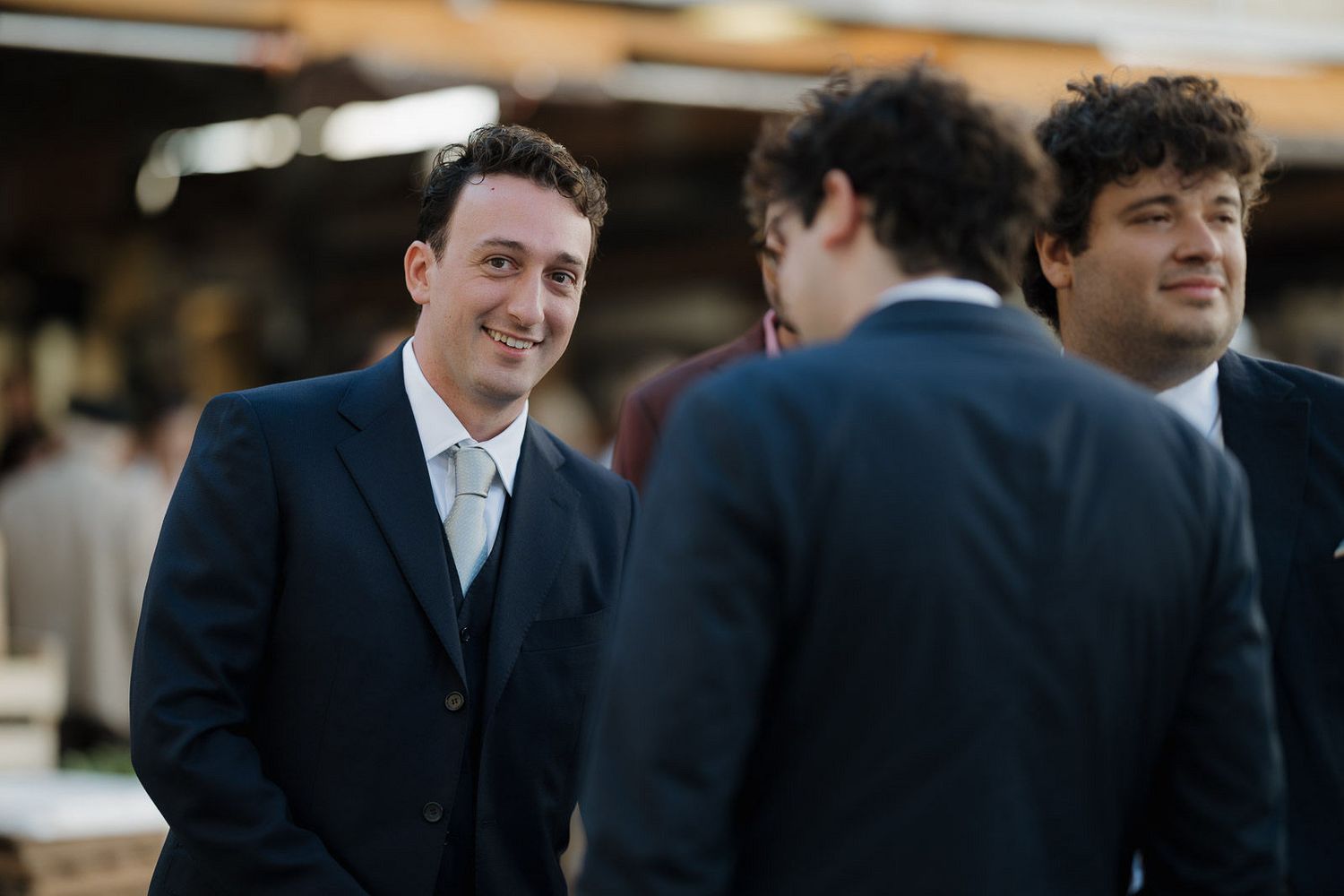 A group of people wearing formal attire smile and interact during a wedding celebration.