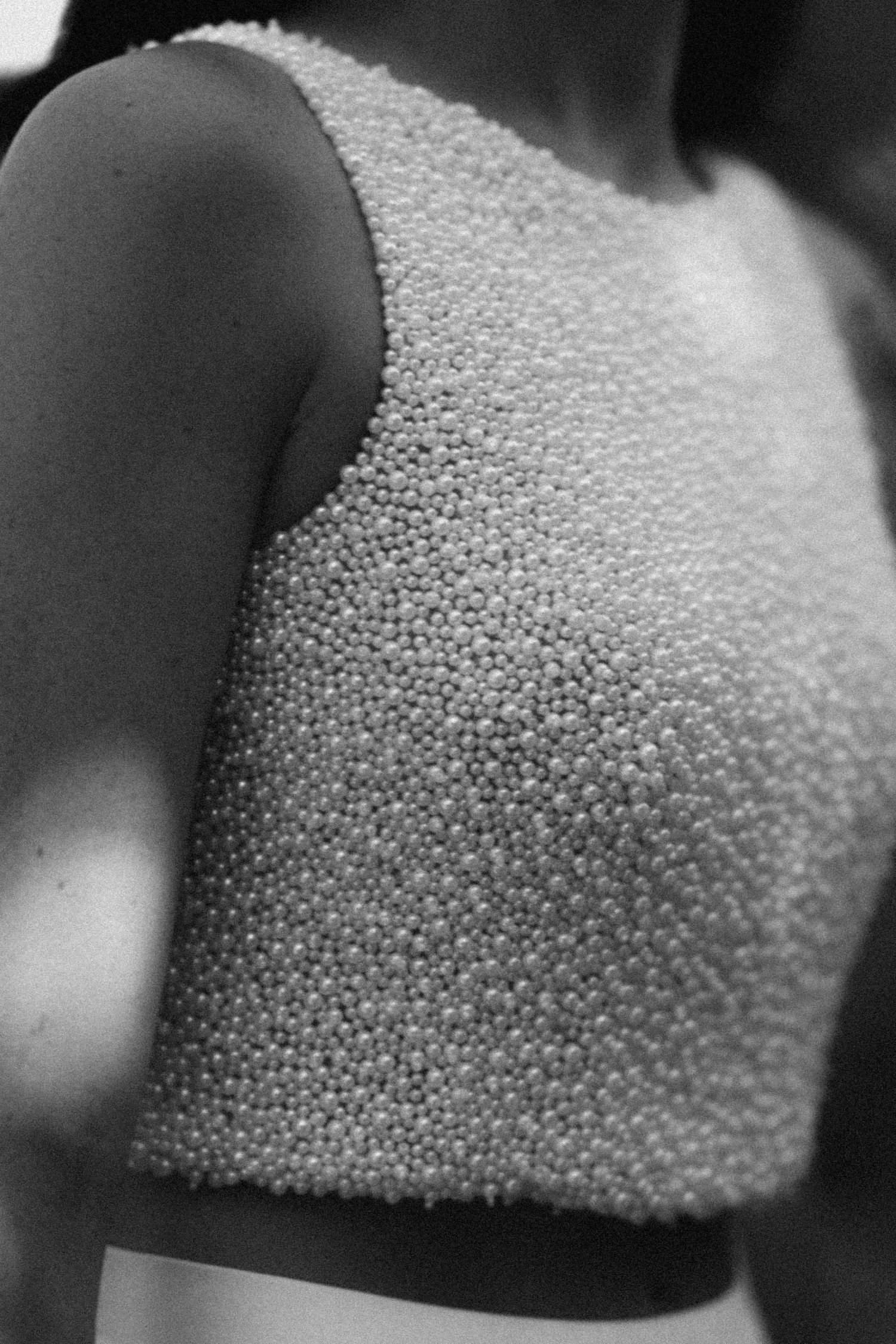 Black and white photo of a woman wearing a sleeveless crop top covered in small pearl beads.