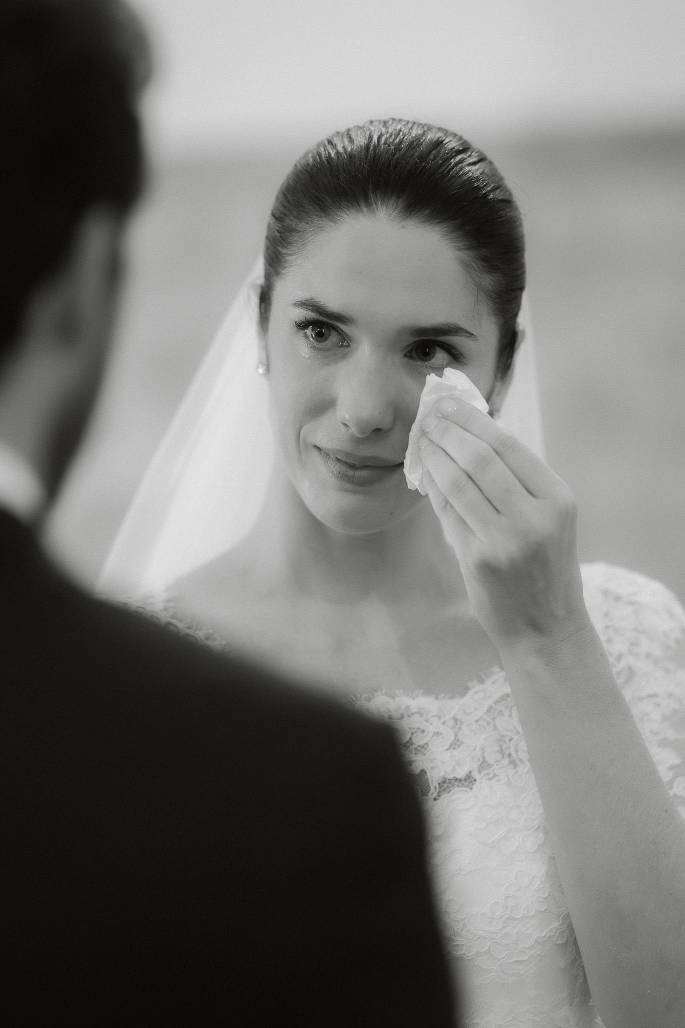 Black and white photo of an emotional bride wiping tears during her wedding ceremony while facing the groom.