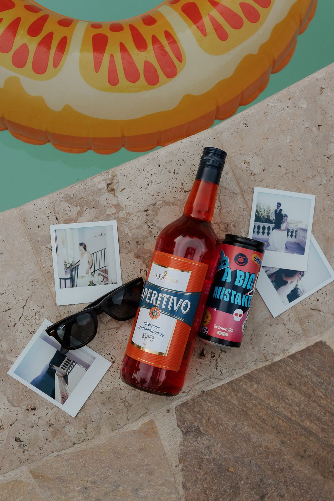 Bottles of colorful cocktails and spirits displayed on a textured stone surface with polaroid photos and sunglasses.
