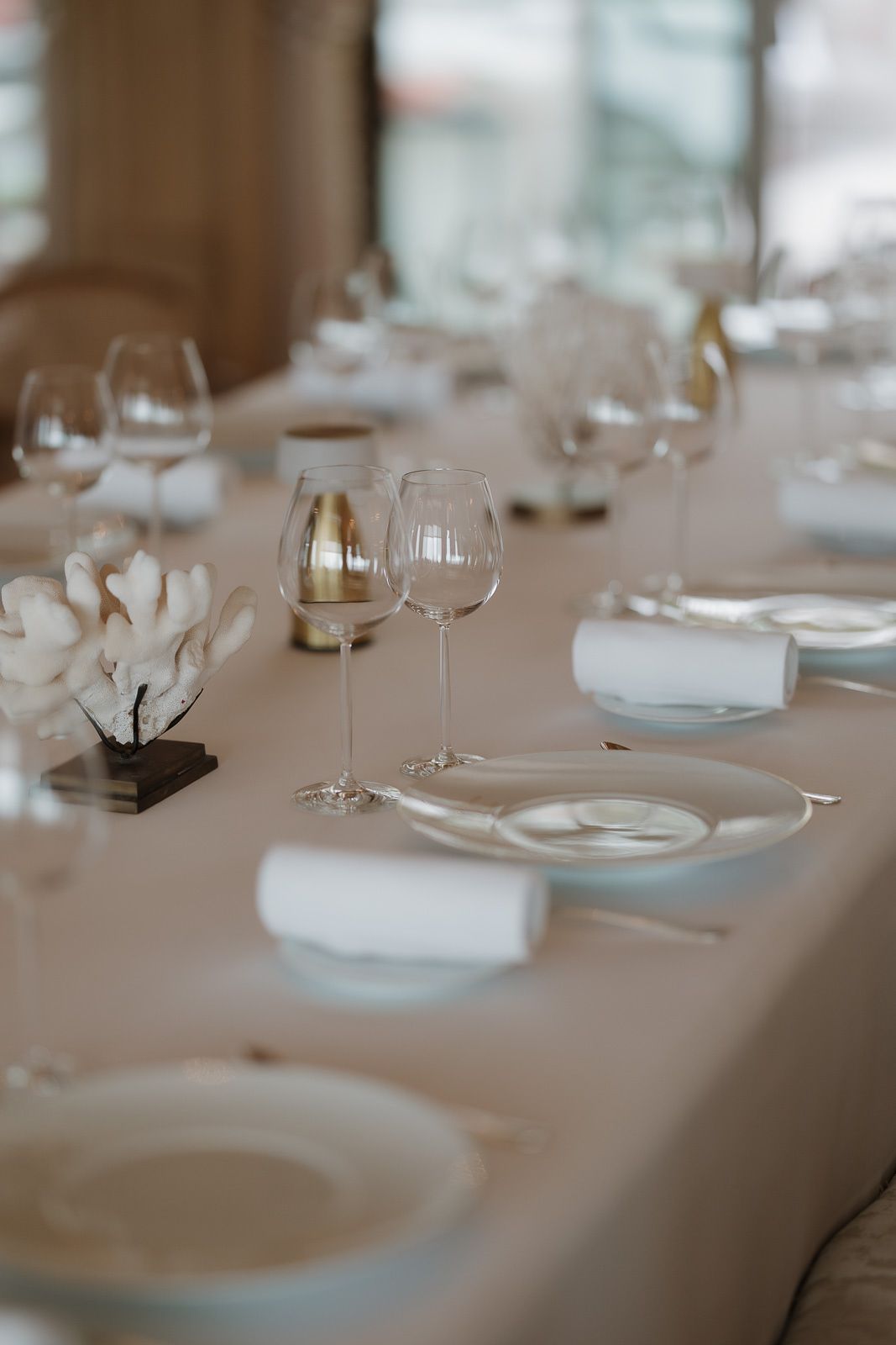 Elegant table setting with wine glasses, white plates, and delicate floral centerpieces on a neutral tablecloth.