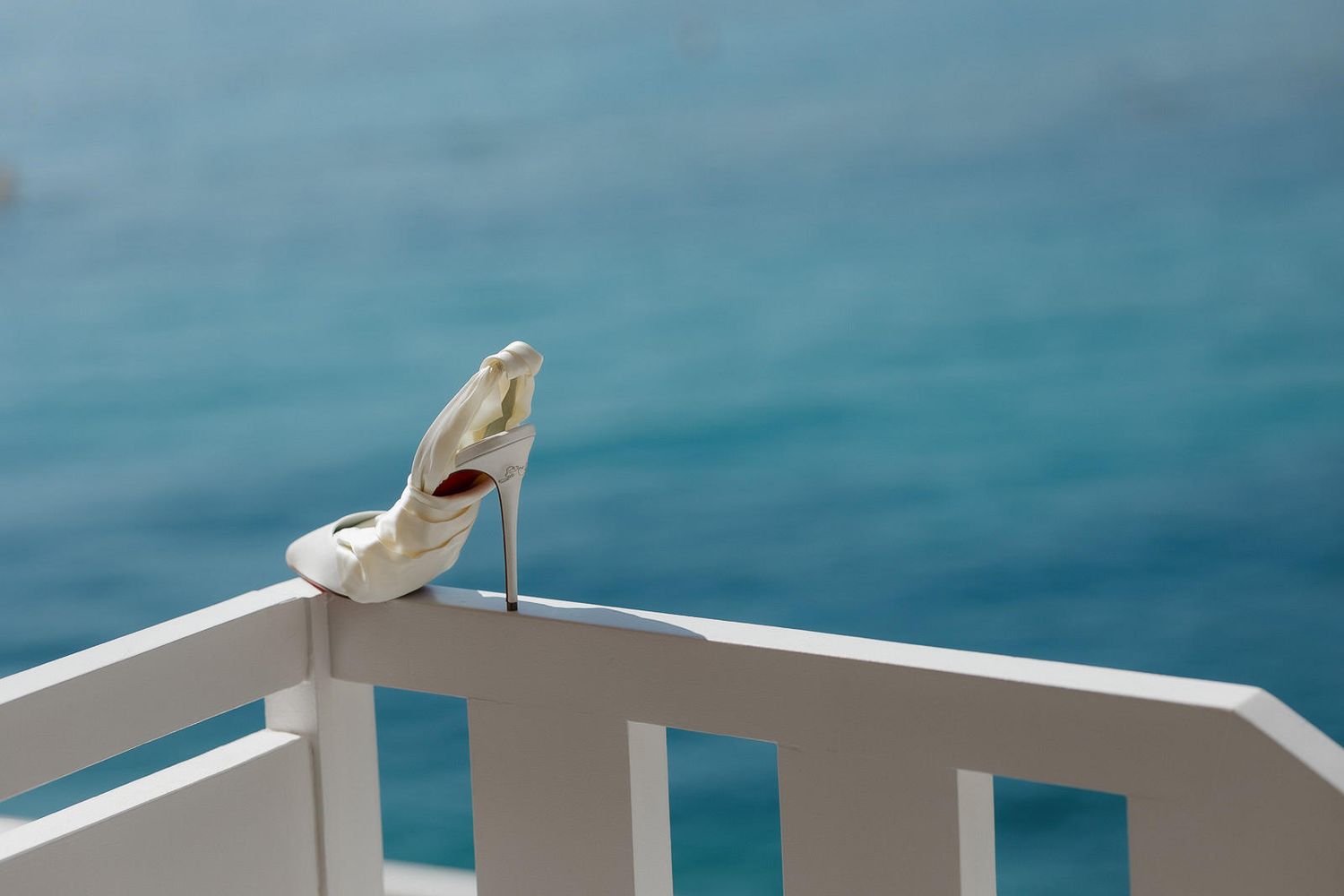 A white seagull perches on a wooden railing against a turquoise ocean backdrop.