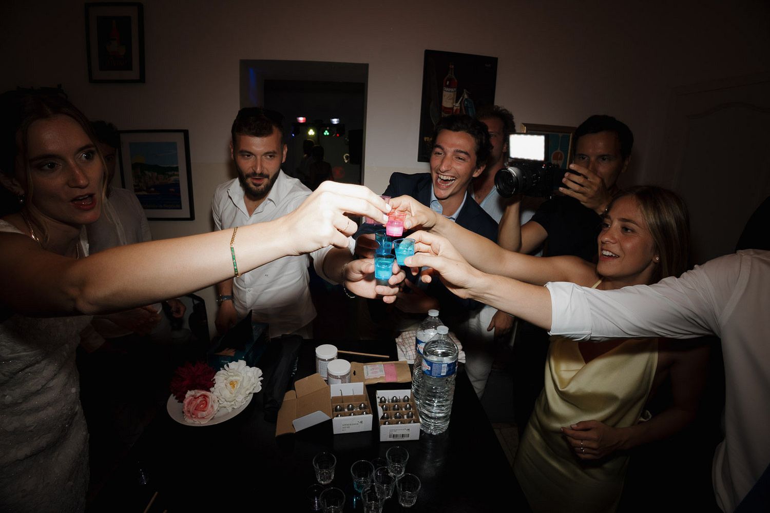 People in a dark room celebrating and raising drinks together in a social gathering atmosphere.