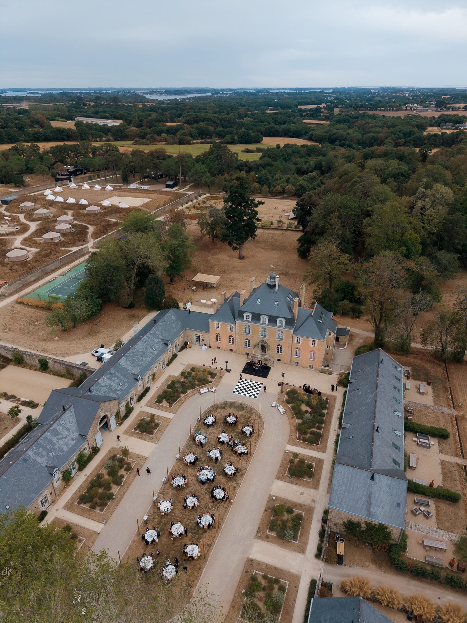 Aerial view of a grand French château with formal gardens, white event tables, and expansive parkland beyond.