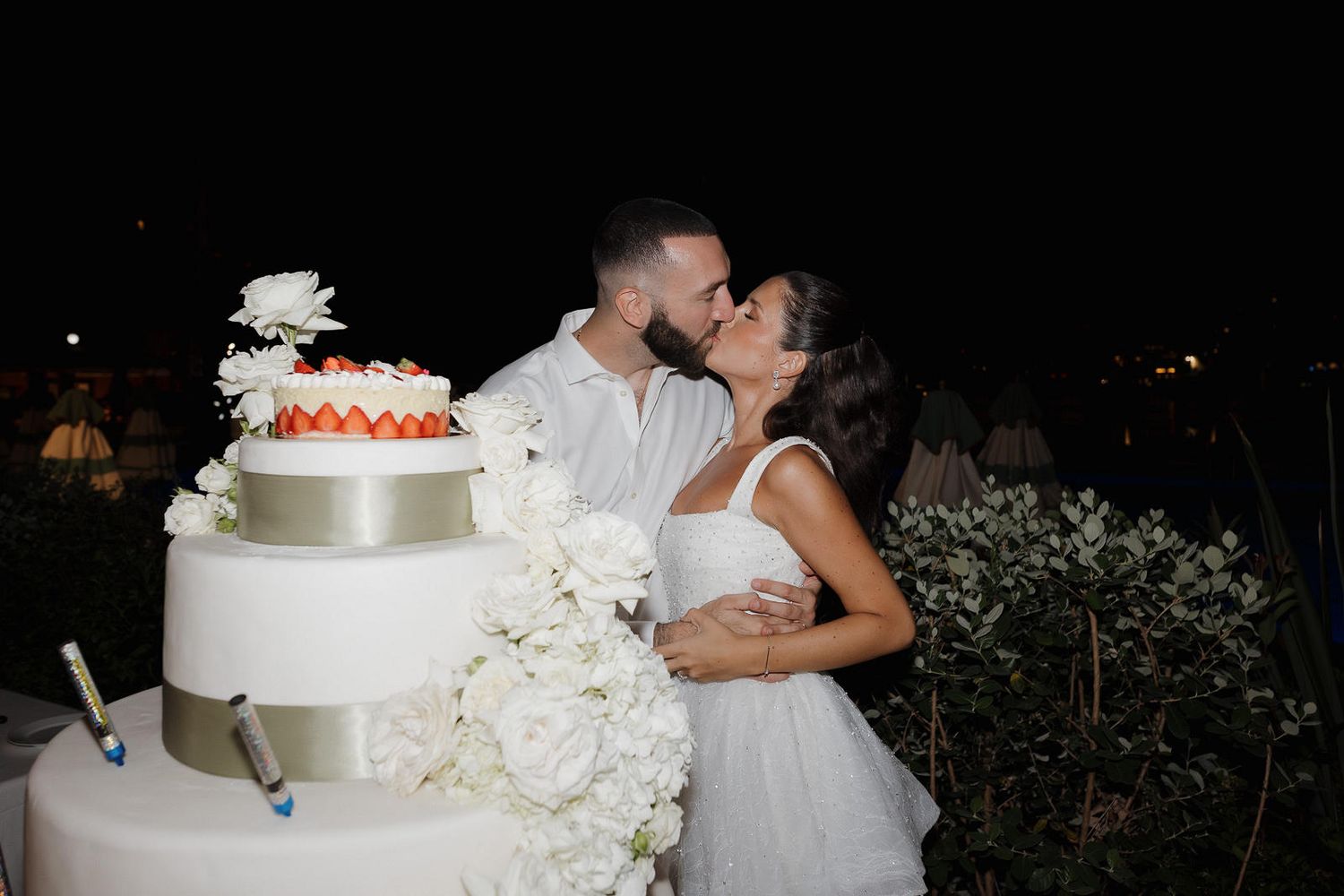A sequence of wedding photos showing cake cutting, kissing moments, and white floral decorations at a romantic reception.