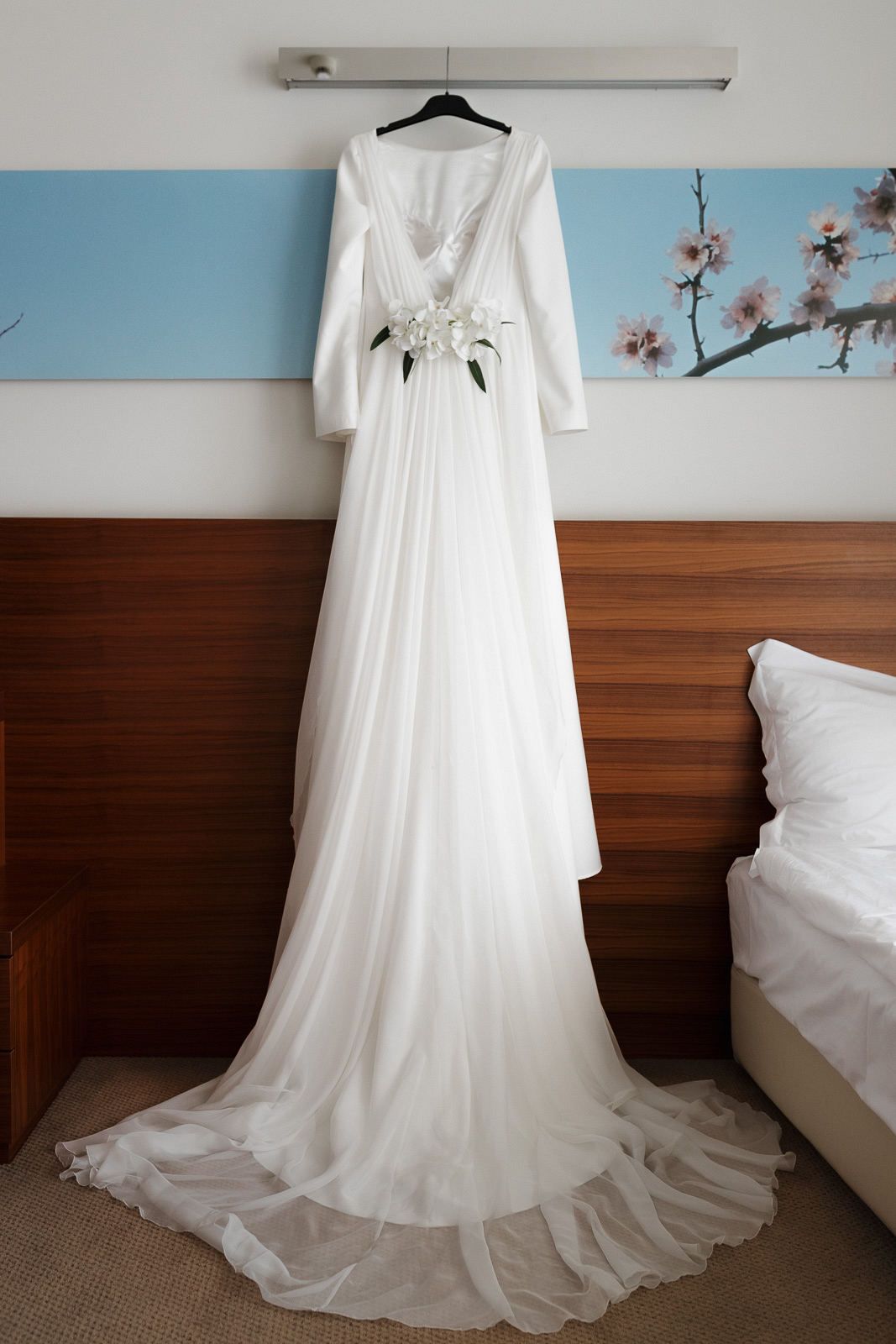 An elegant white wedding dress with long train displayed on a hanger against wooden paneled walls.