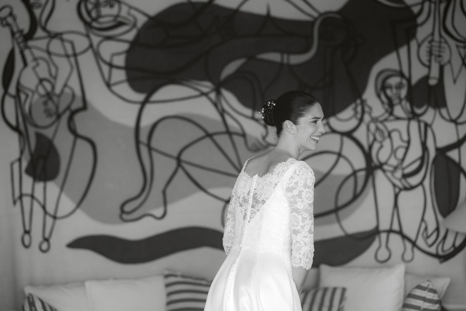 Bride in lace wedding dress smiling before abstract mural wall in black and white photo.