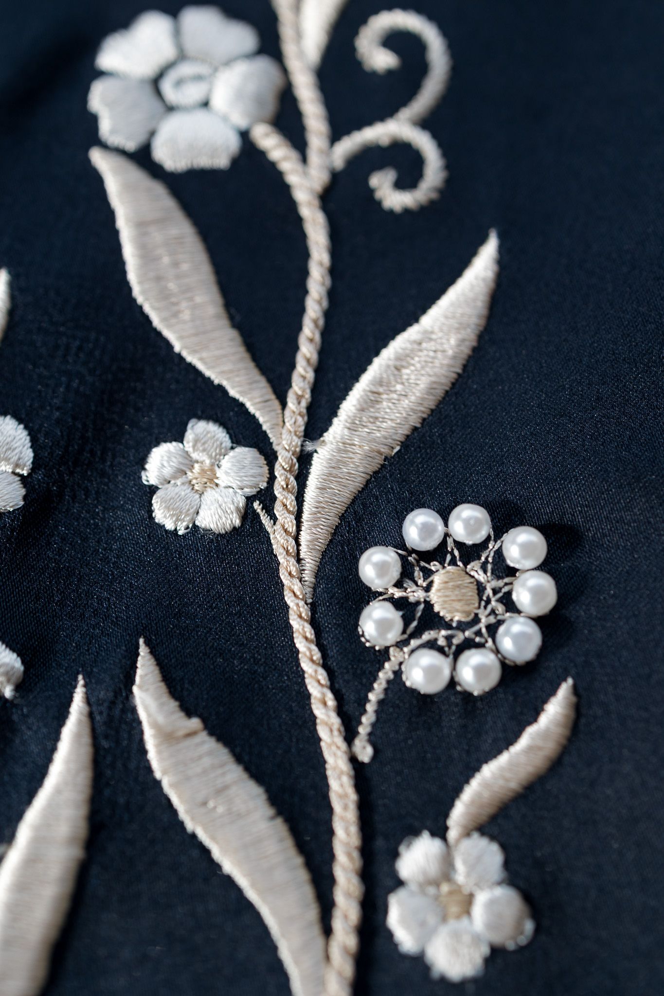 Close-up of white floral embroidery and pearl brooch on dark navy fabric.