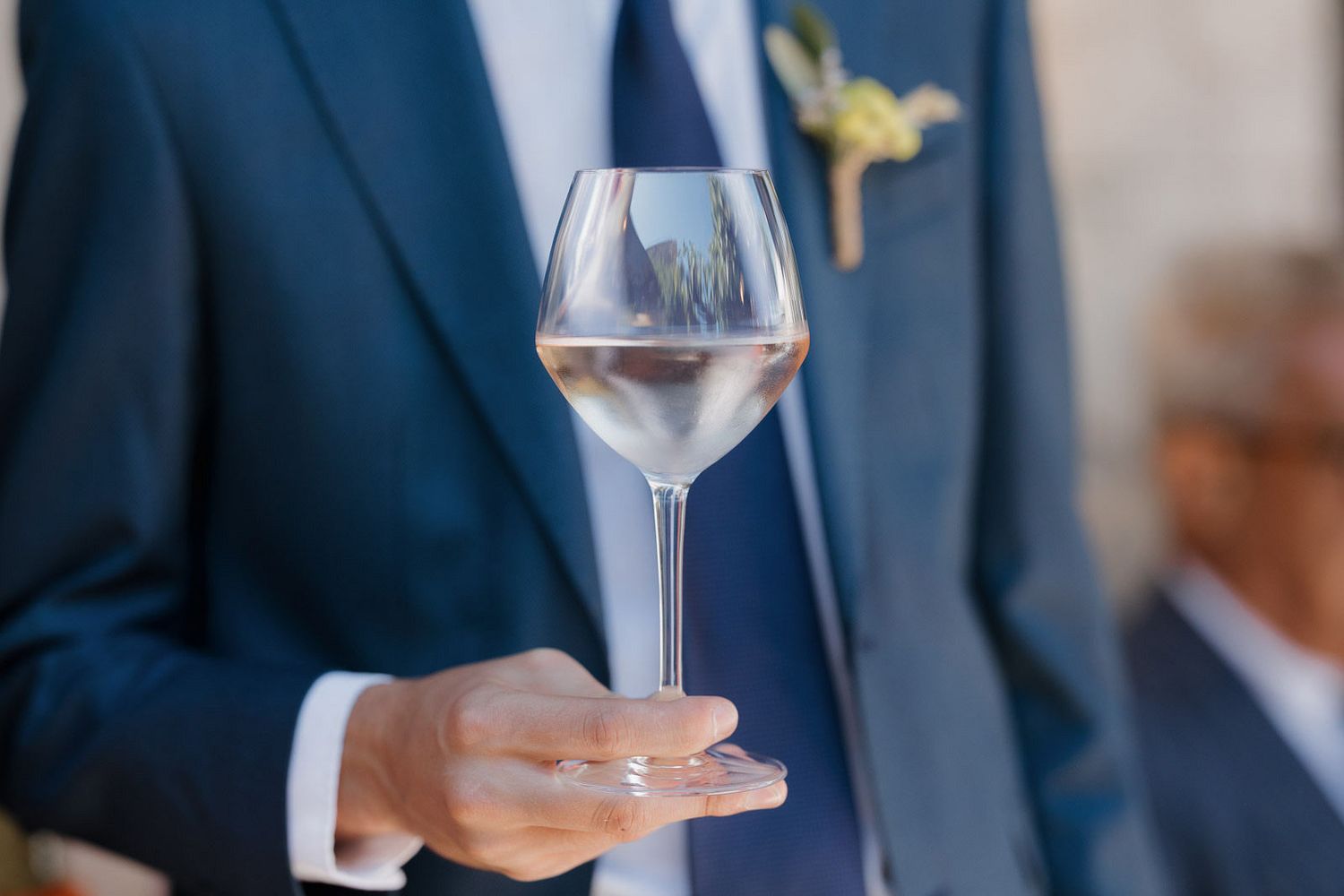People holding wine glasses at an elegant event while wearing formal attire and navy blue suits.