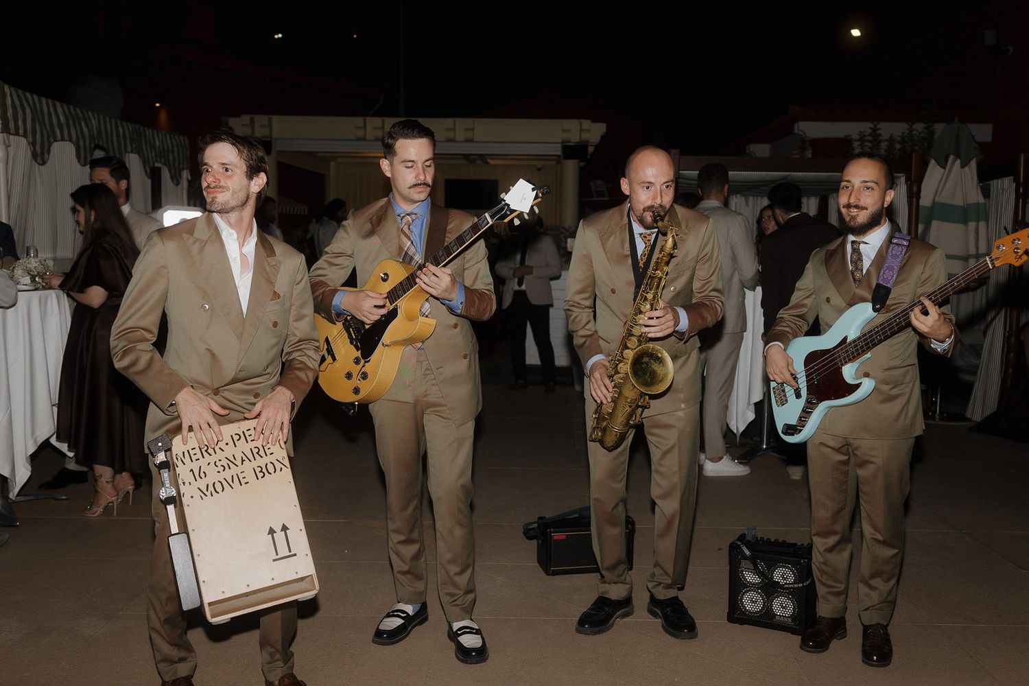 Musicians in tan suits perform with saxophones and other instruments during an evening event.