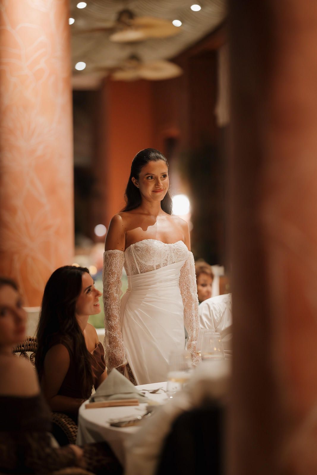 Candlelit wedding reception table with guests seated in an elegant restaurant setting with warm lighting and columns.