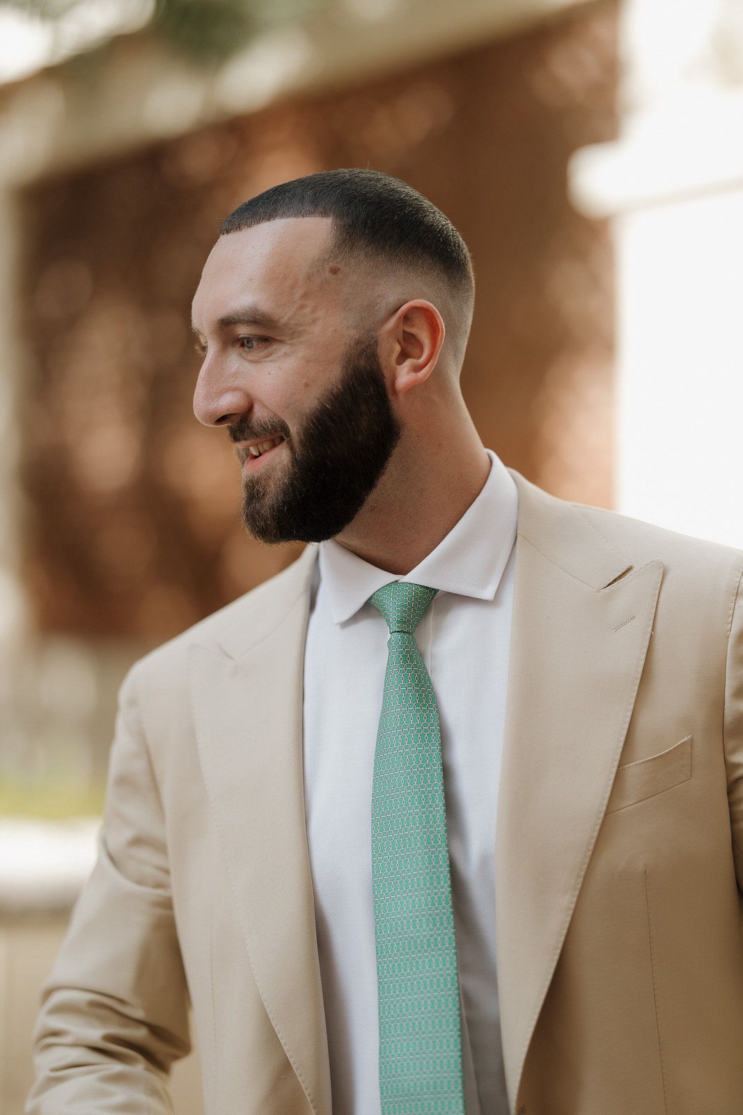 A person wearing a beige suit and mint green tie smiles in a series of candid portrait shots.