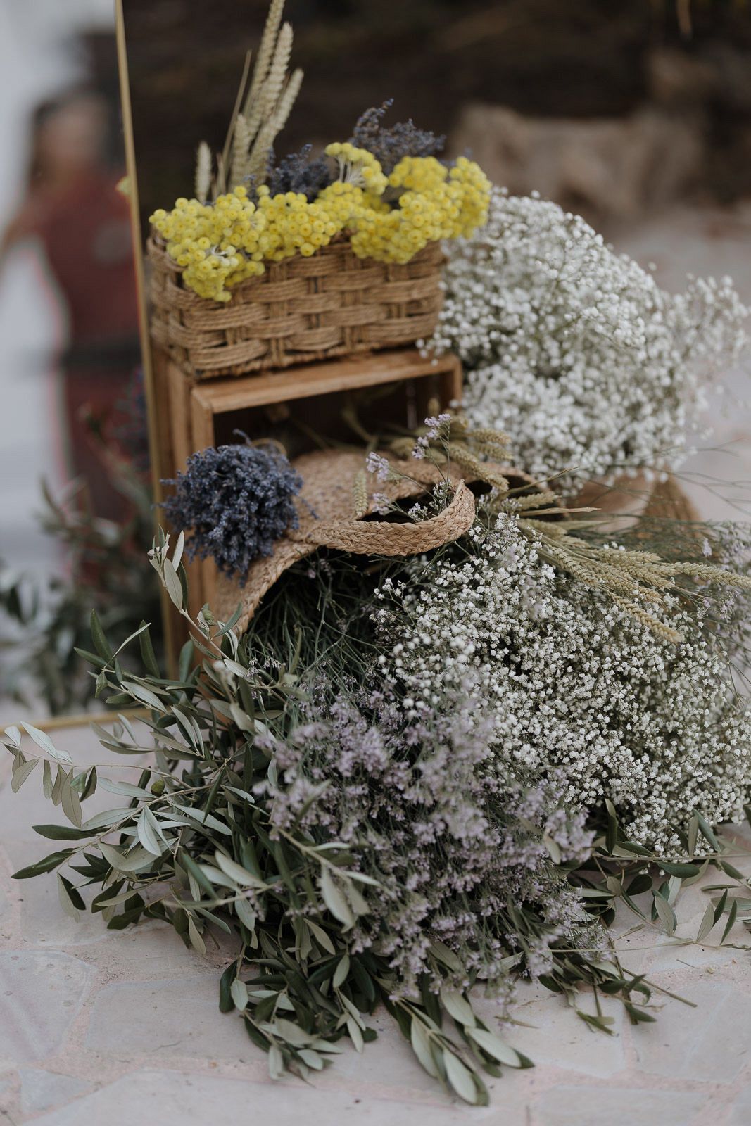 Rustic wooden crates filled with yellow flowers and baby's breath alongside delicate olive branches and greenery.