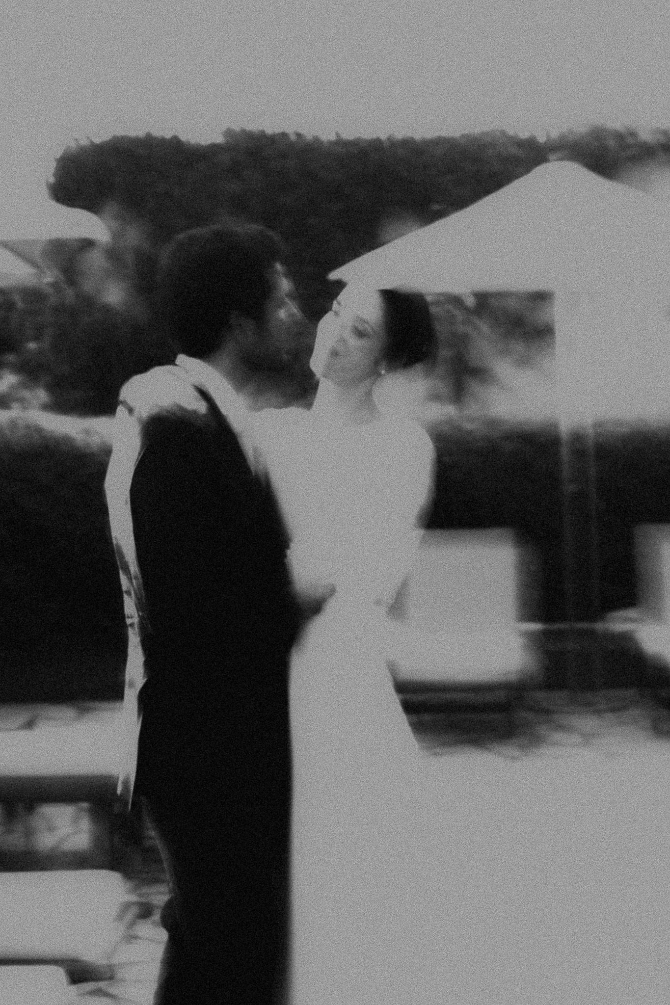 Black and white blurry photo of a couple in wedding attire embracing outdoors.