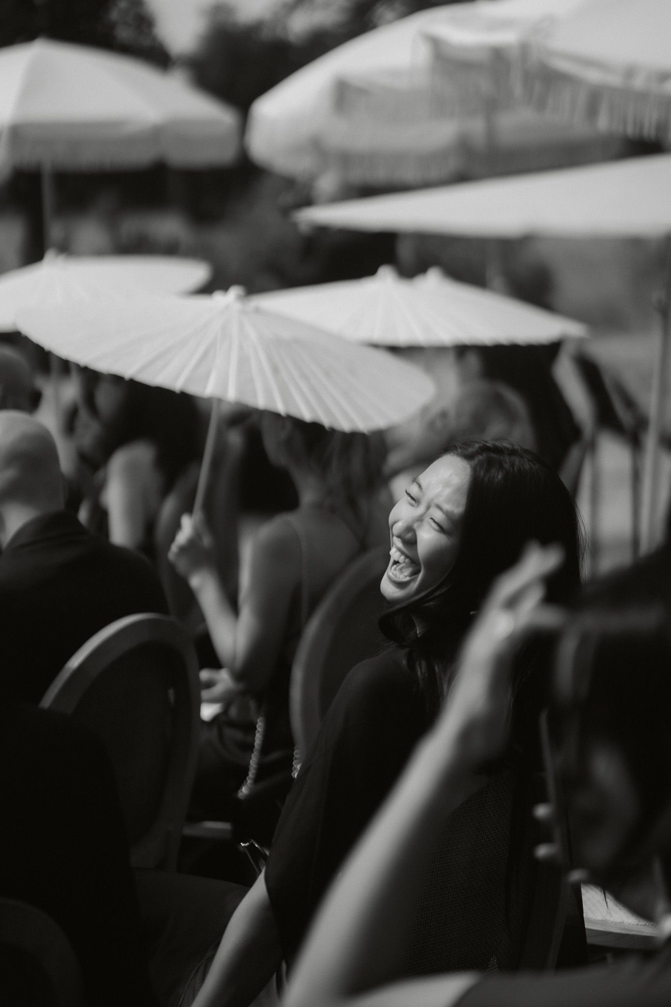 A woman laughs joyfully at an outdoor event surrounded by white parasol umbrellas.