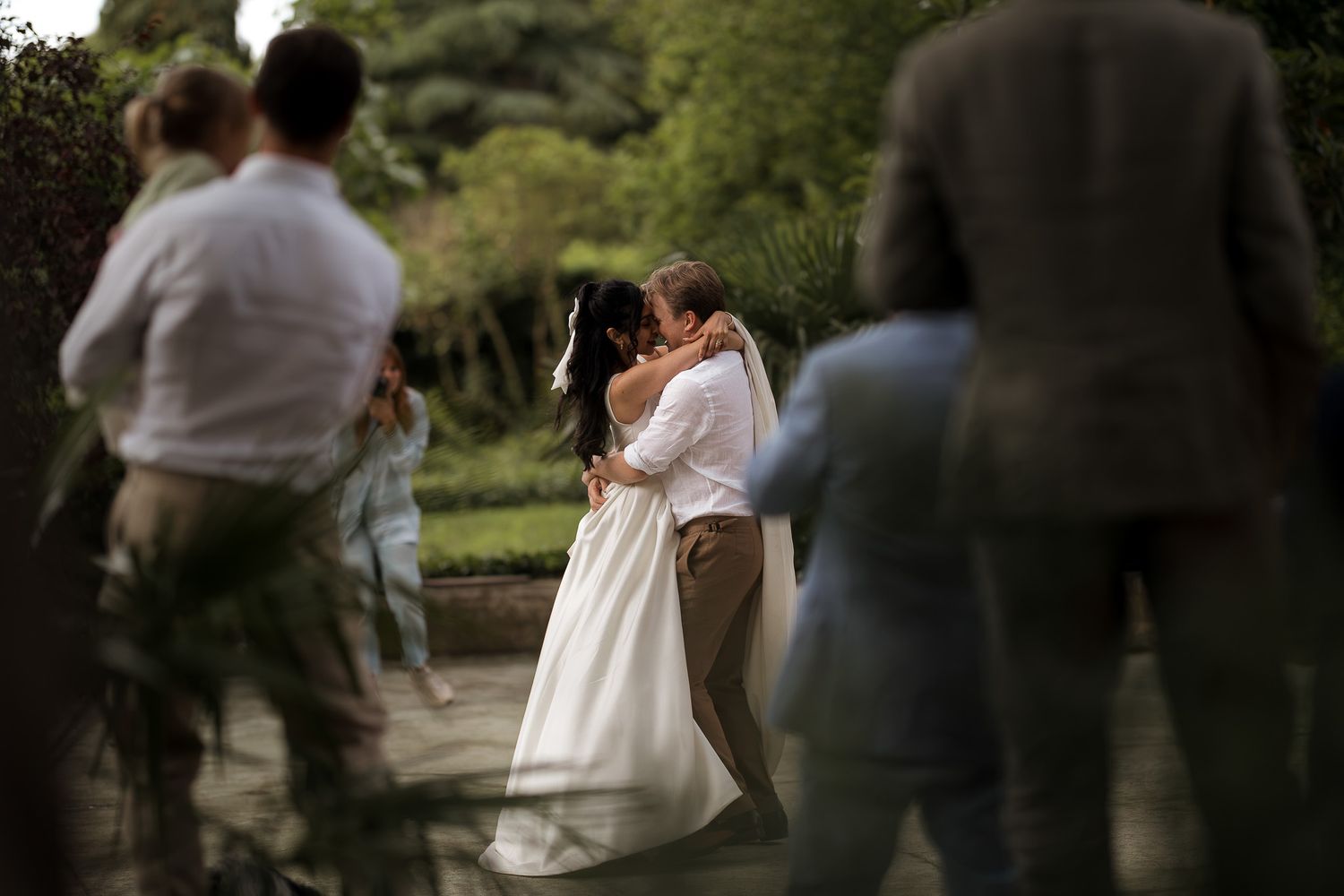 Bride and groom share a romantic kiss outdoors at a garden wedding surrounded by guests.