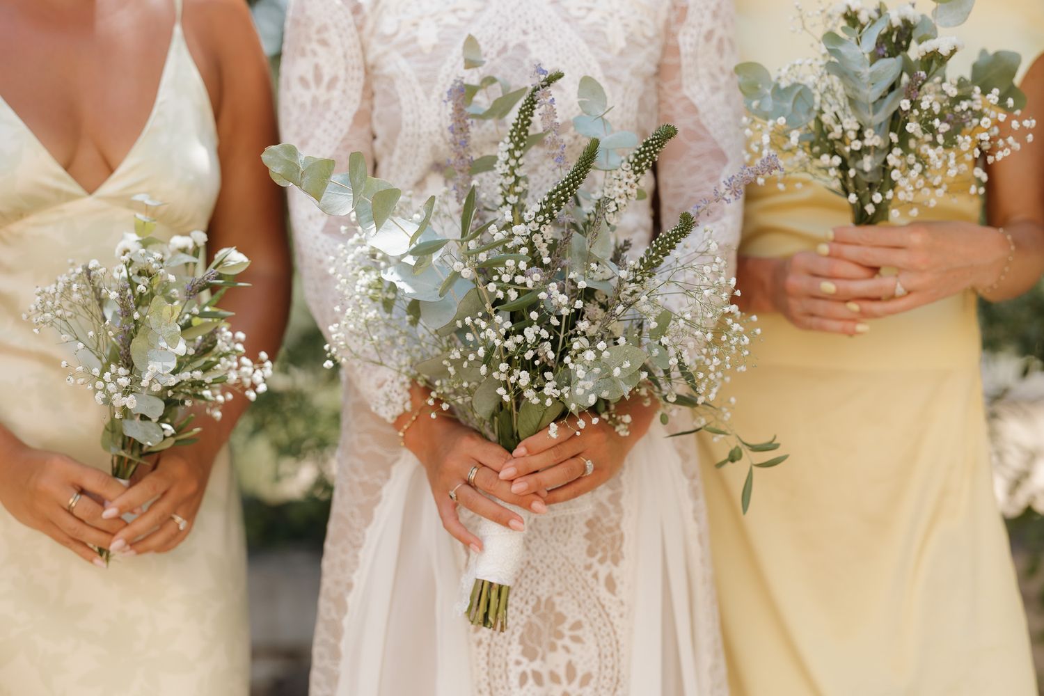 Bride and bridesmaids holding eucalyptus and baby's breath bouquets in white and yellow dresses.
